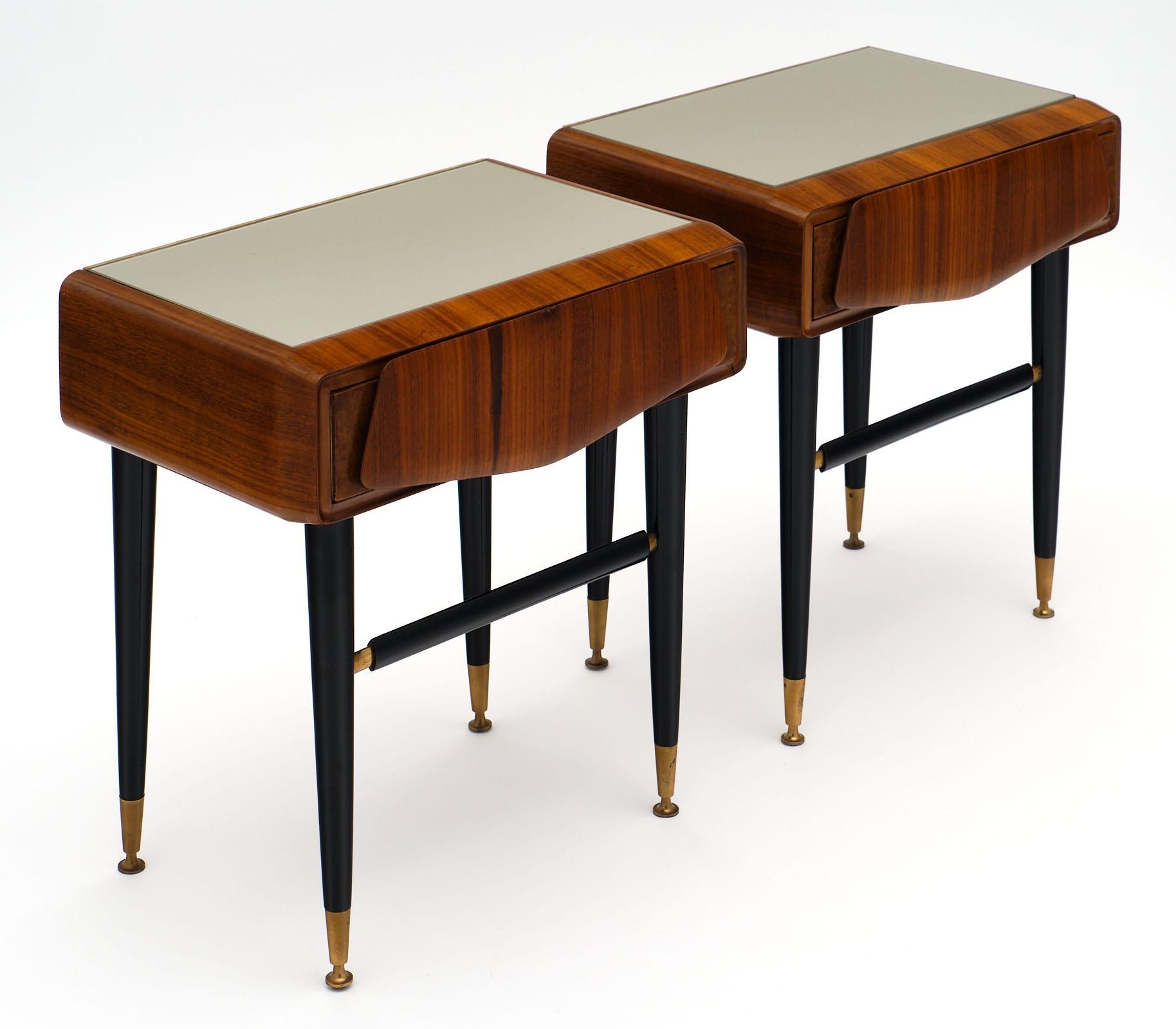 Italian midcentury side tables each featuring a drawer and a gray colored glass top. The base is ebonized with gilt brass accents. We love the sleek details and lines of this pair.