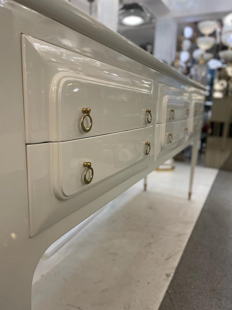 Stylish Mid Century Modern 1950s Italian Sideboard/Credenza in Ivory Lacquered Wood. The top of the sideboard has a green glass decorated with hand-painted gold decorations, with 6 drawers and brass feet. 



 