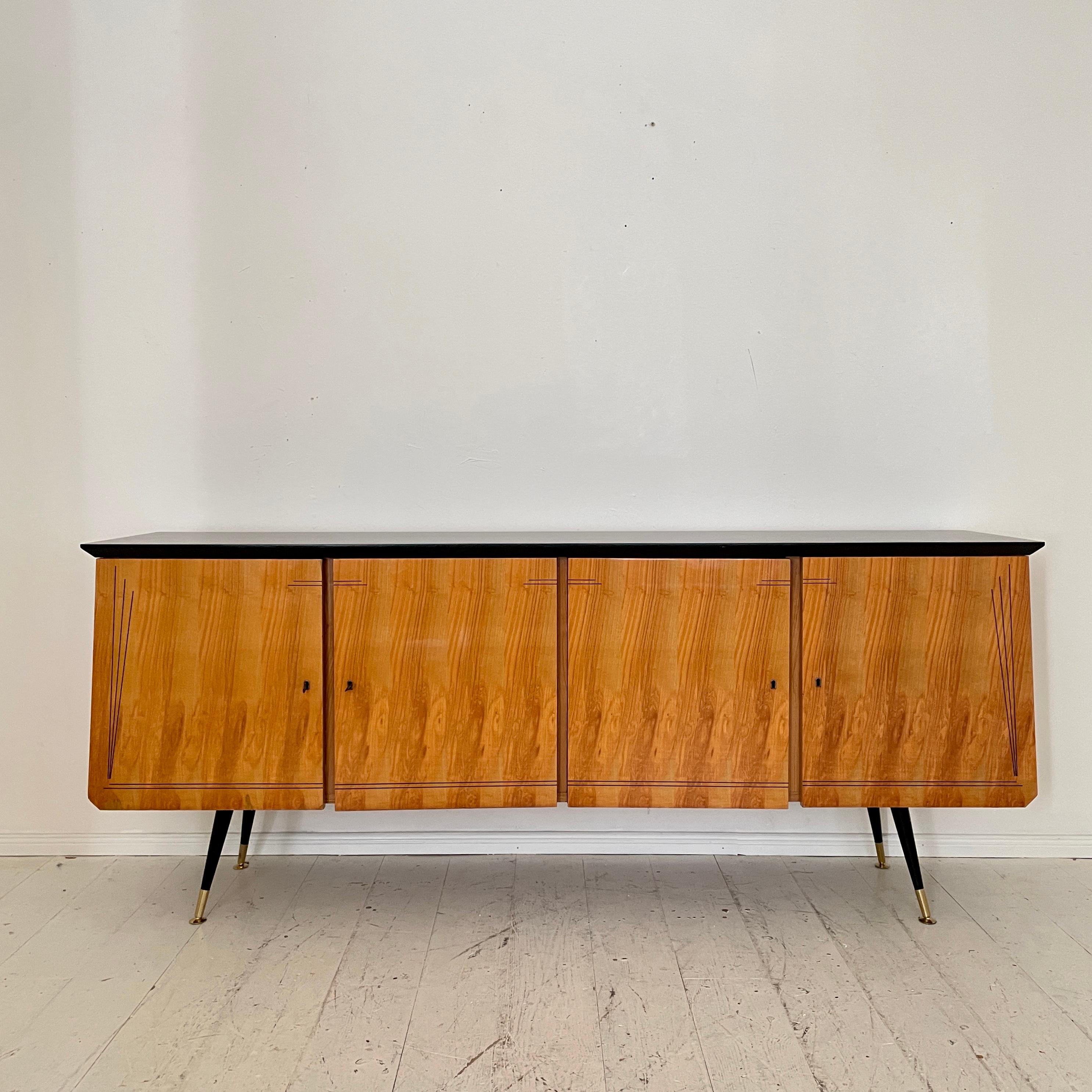 This beautiful Italian midcentury Sideboard was made around 1950.
It has got 4 Doors and is veneered in ash, and the top is lacquered black. The black lacquered tapered legs have got brass shoes.
A unique piece which is a great eye-catcher for