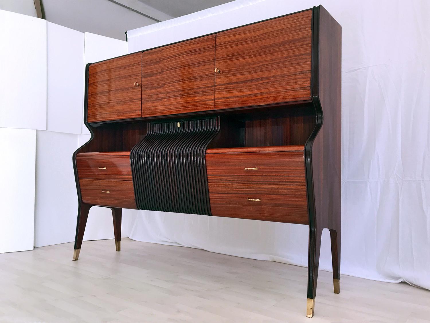 Stylish sideboard and/or bar cabinet designed by Osvaldo Borsani in the 1950s.
Its structure is characterized by a unique shape design given by its amazing curved frontal profile of the central drop-down door, very refined and finished with