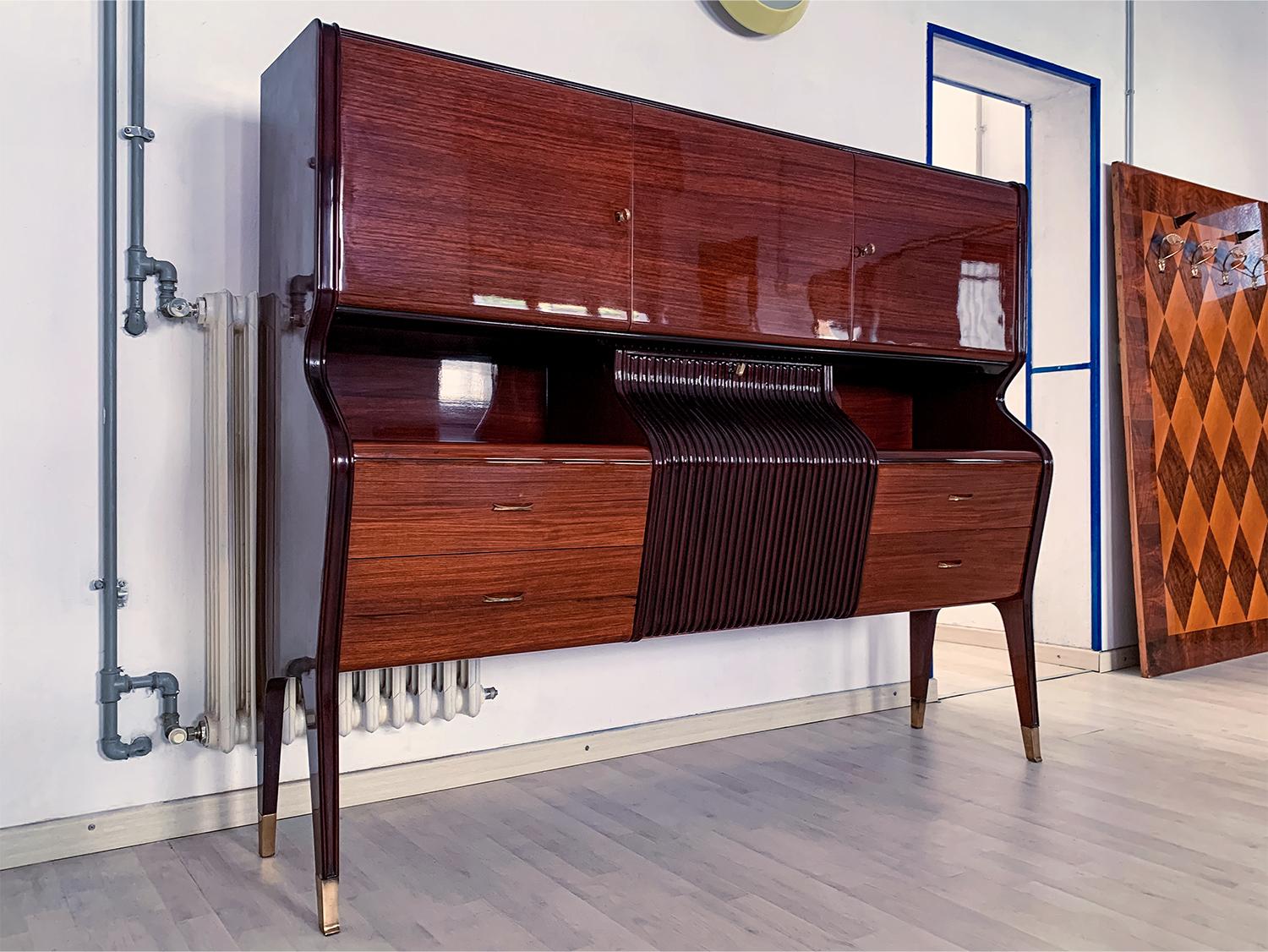 Stylish sideboard and/or bar cabinet designed by Osvaldo Borsani in the 1950s.
Its structure is characterized by a unique shape design given by its amazing curved frontal profile of the central drop-down door, very refined and finished with