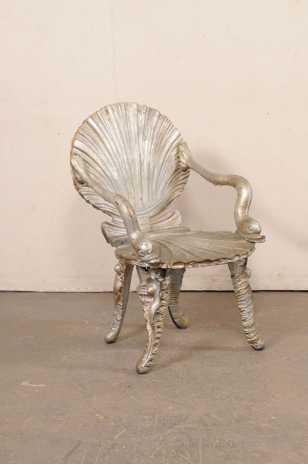 An Italian carved wood grotto chair, in shell and dolphin motif, from the mid 20th century. This mid-century grotto chair from Italy is an ocean-themed piece with shell-carved backrest and seat (as if an open clamshell), dolphin arms, and four legs