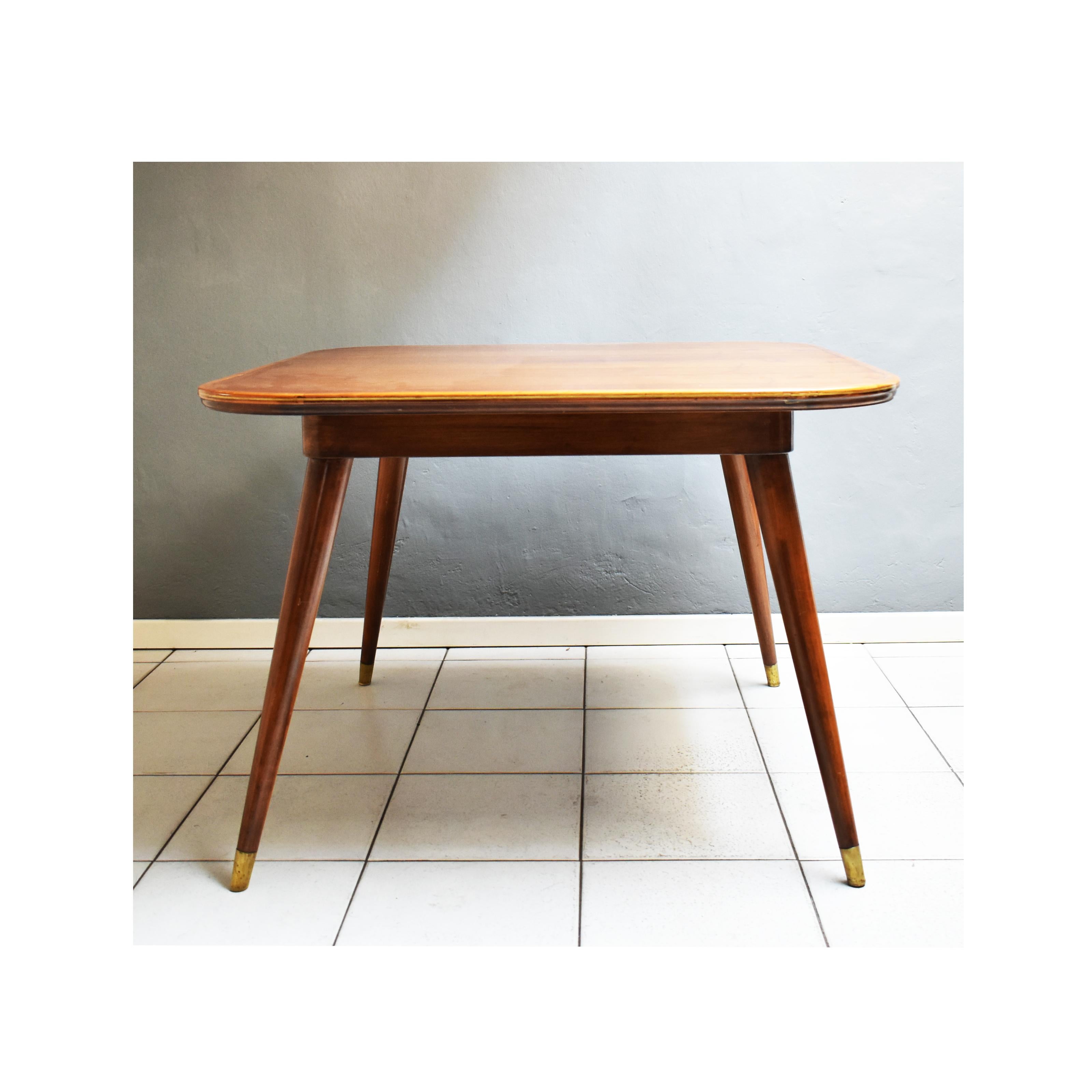 Table vintage des années 1950, fabrication italienne.
La table a une structure carrée avec des bords arrondis. 
Le long du contour de la surface d'appui, le bois présente une bordure en laiton qui est répétée sur le dessus et dans la partie finale