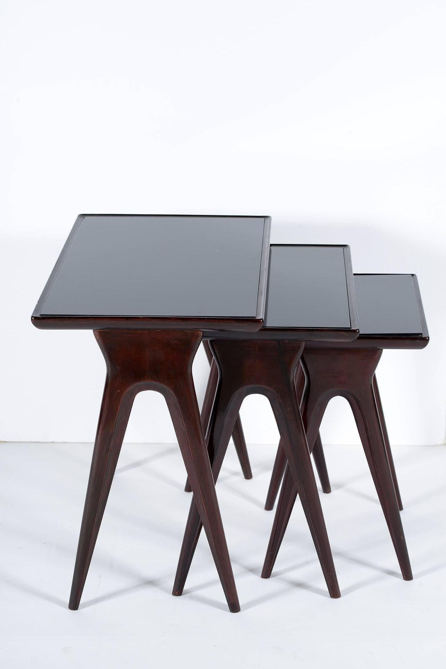 Three nesting tables with slender legs in dark wood and black glass top.
The listing measures are when the tables are stacking and closed.

 