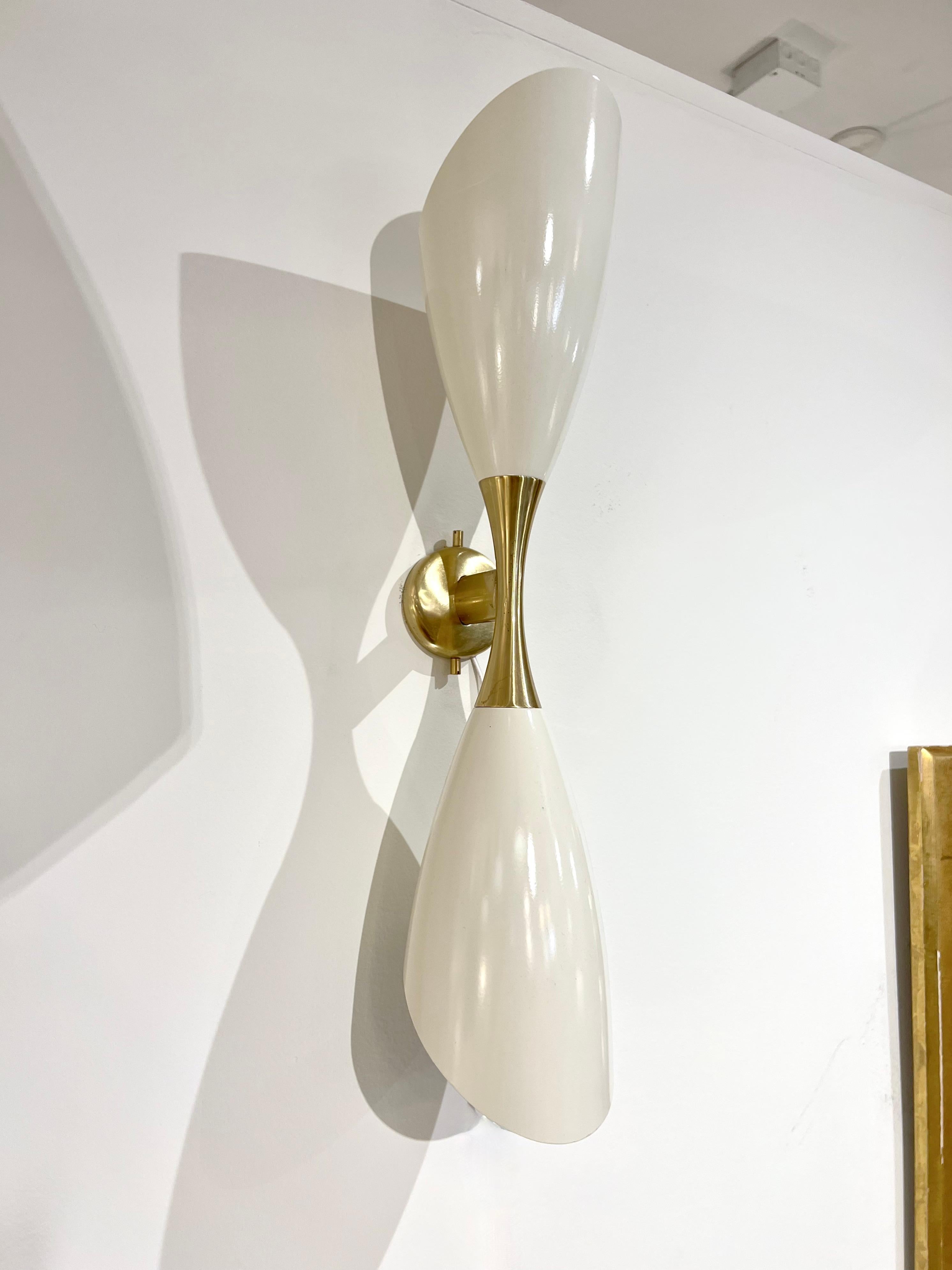 An impressive contemporary sconce in the style of the classic designs of the Mid Century period. Made in Italy, contemporary.
Made in brass and off-white enamel covered metal shades with two sockets.
