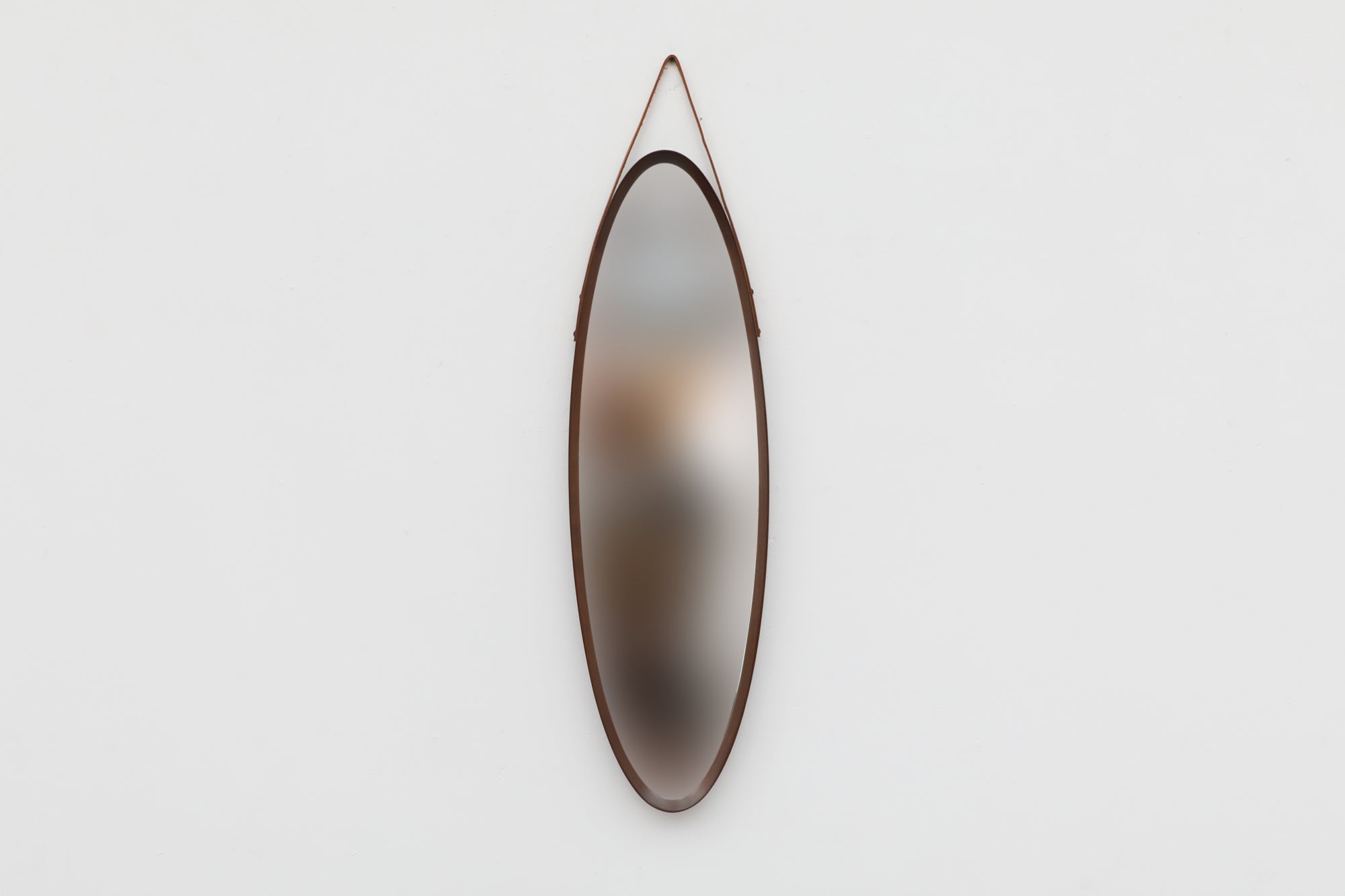 Italian Mid-Century oval wall mounted mirror with teak frame and leather strap in the style of Jacques Adnet. Beautiful solid bent teak framing, in original condition with some wear consistent with its age and use. Other similar mirrors available
