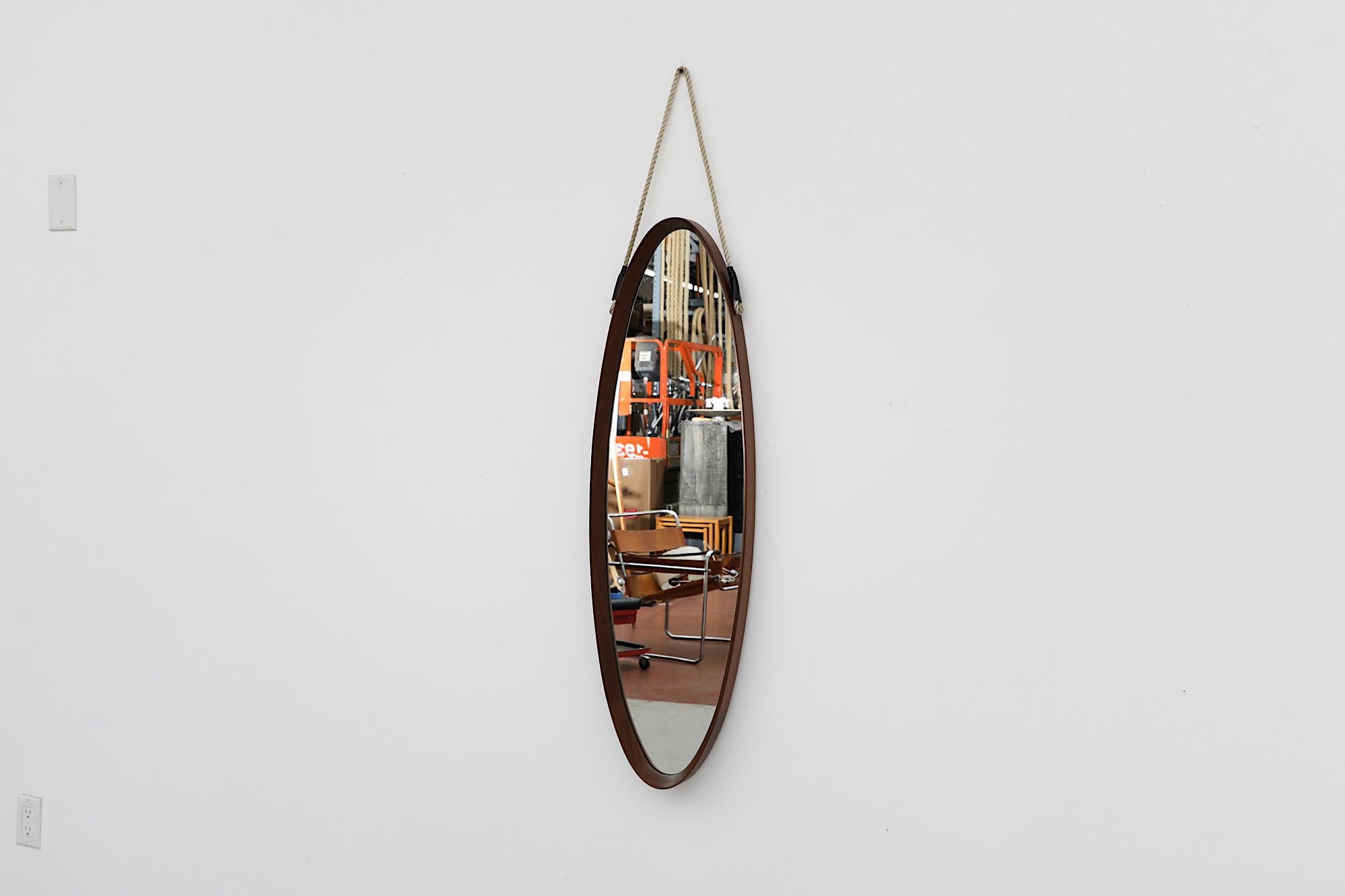 Italian Mid-Century long oval wall mounted mirror with heavy bent teak frame and rope strap. In original condition with visible wear consistent with its age and use. Other similar mirrors available and listed separately.