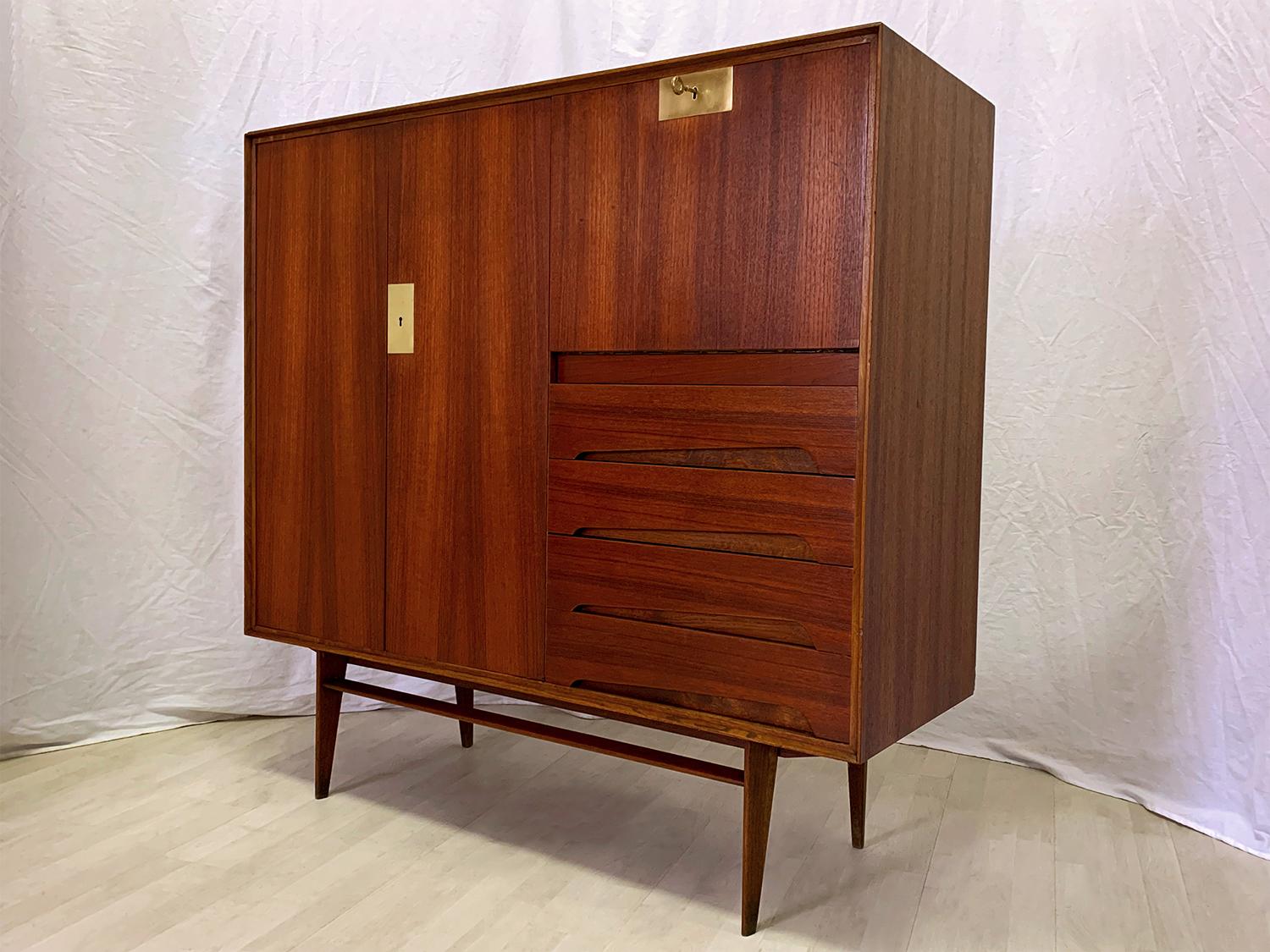 Stunning sideboard crafted with a gorgeous material like as warm teakwood, finished with brass details, and its uniqueness is given by the presence of a drop-leaf door on the right side, that makes it available as a secretaire.
Its doors and