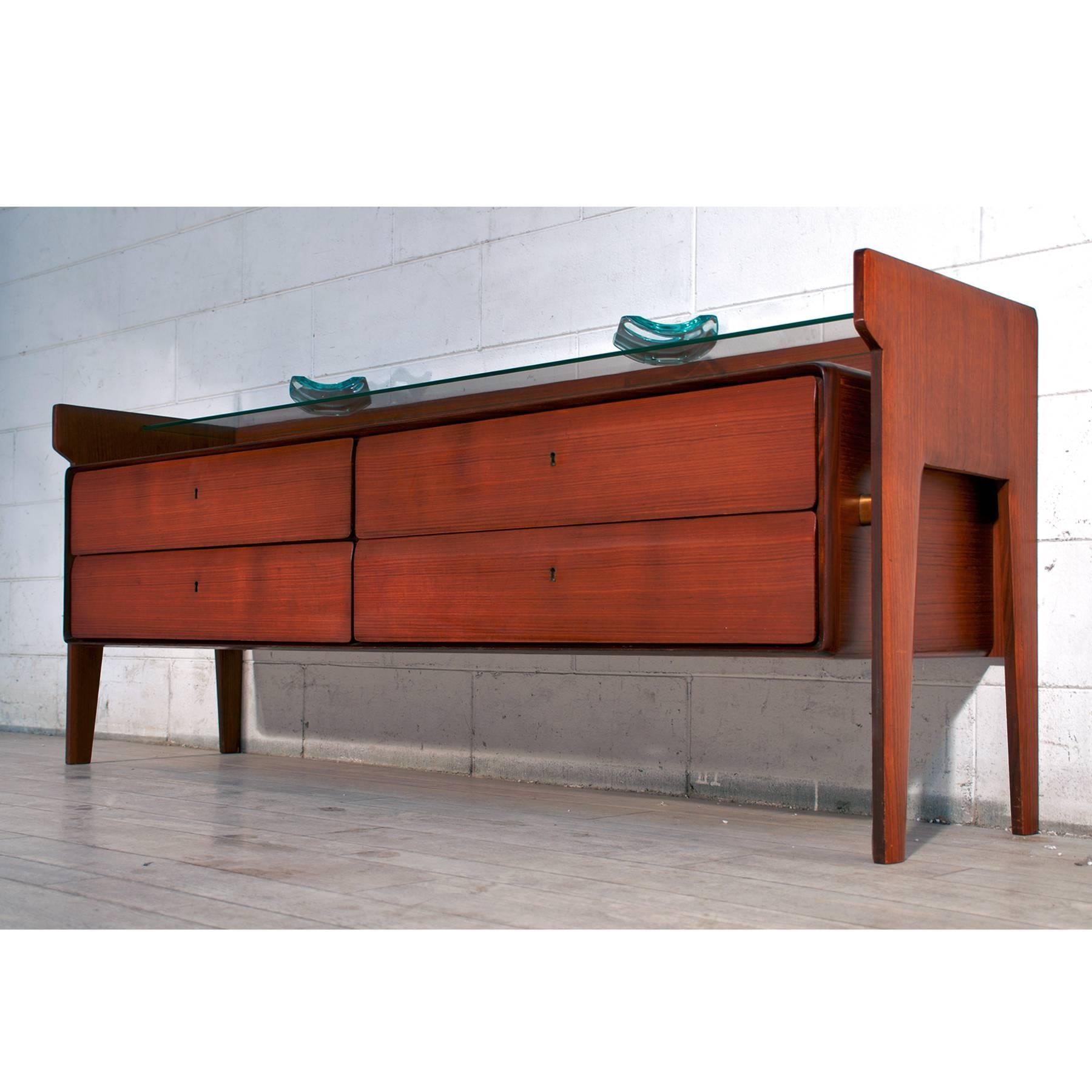 Stylish Italian dresser of the 1950s, made in gorgeous material like teak wood veneered in reddish tint, finished with brass details and equipped with a suspended glass shelf and four drawers.
Its conditions of the period are very good as the images