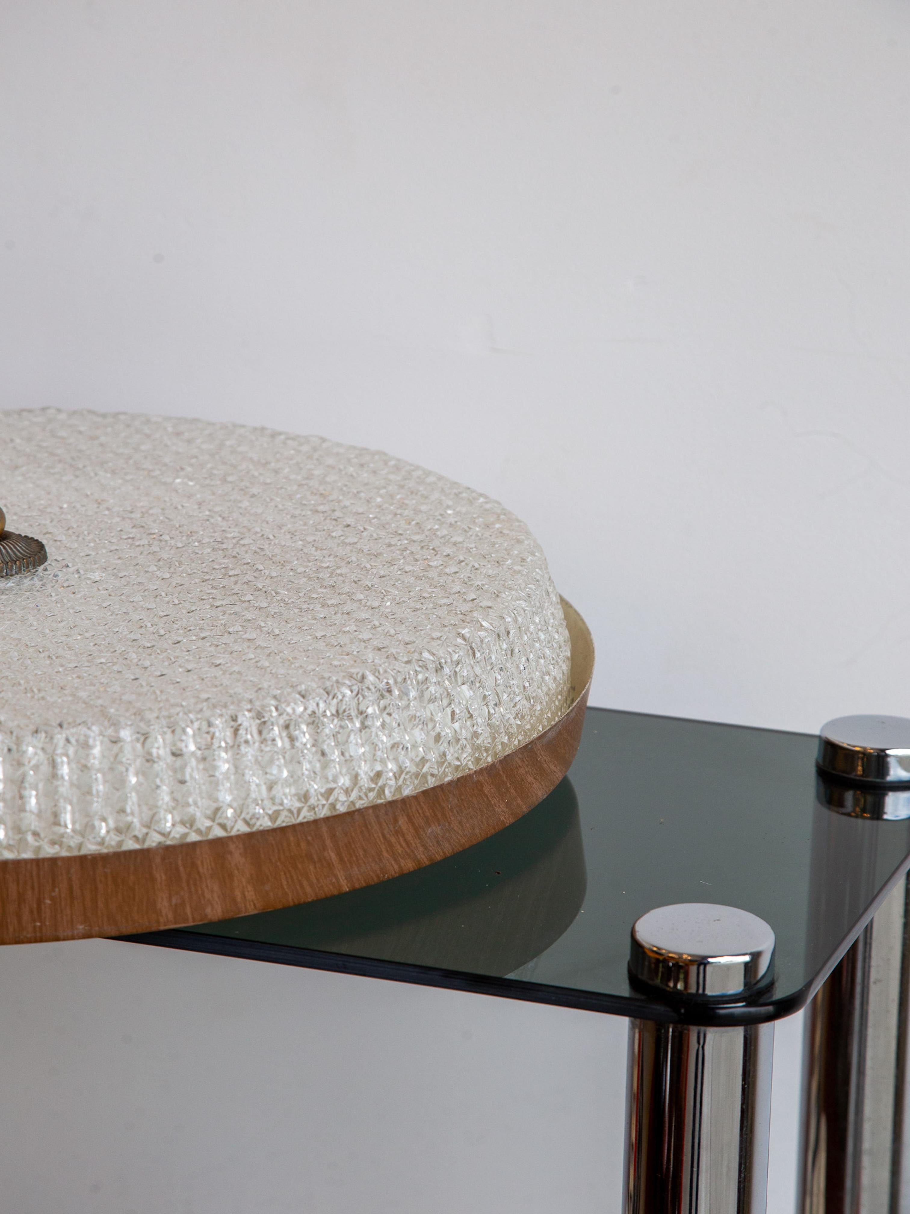 Raffinato esempio di design italiano di metà secolo, questa plafoniera degli anni '50 presenta un diffusore in vetro riccamente strutturato montato su una struttura in ottone e legno dai toni caldi. La superficie convessa del vetro è intricata con