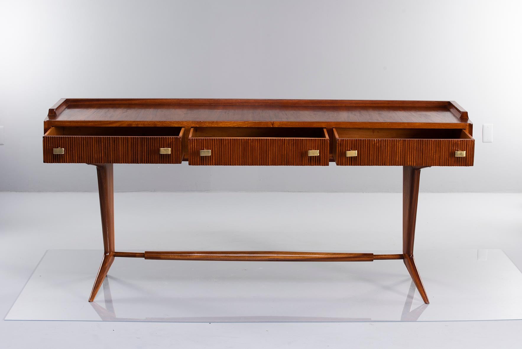 Italian desk with three shallow functional drawers, circa early 1960s. Unknown wood species. Drawers have dove tail construction with ridged fronts and brass hardware. Narrow tapered splayed legs with turned stretcher.