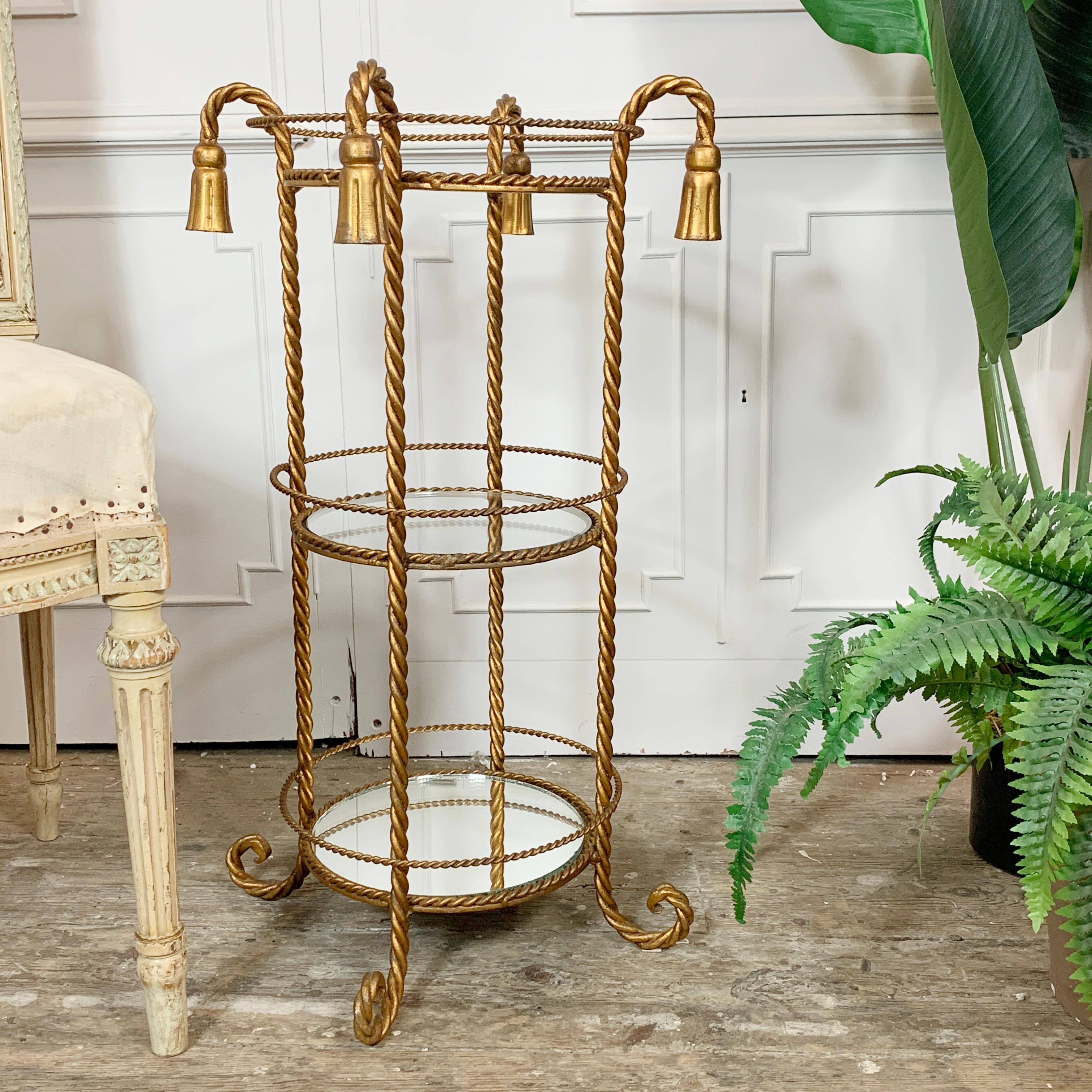 Beautiful twisted gilt iron triple tiered Italian stand, with two glass and a mirrored shelf. Dating to the late 1950's, it sits upon twisted turned feet, and is adorned with four tassels that hang from the twisted gilt legs.

A wonderful size,