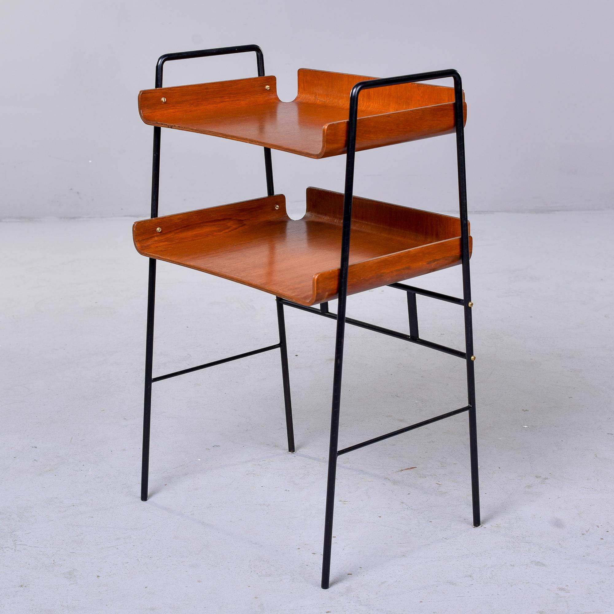 Found in Italy, this two tier wood side table with black iron frame dates from the 1970s. Table has narrow black iron frame with bentwood shelves covered in teak veneer. Unknown maker. Very good vintage condition with minor scattered surface wear.