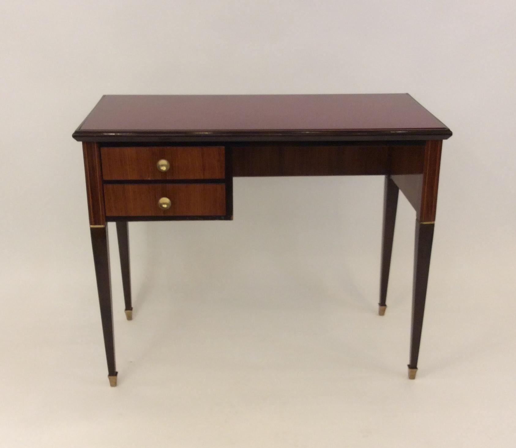 An Italian vanity table/small desk in mahogany with two drawers, brass hardware and red glass top.
In lovely vintage condition