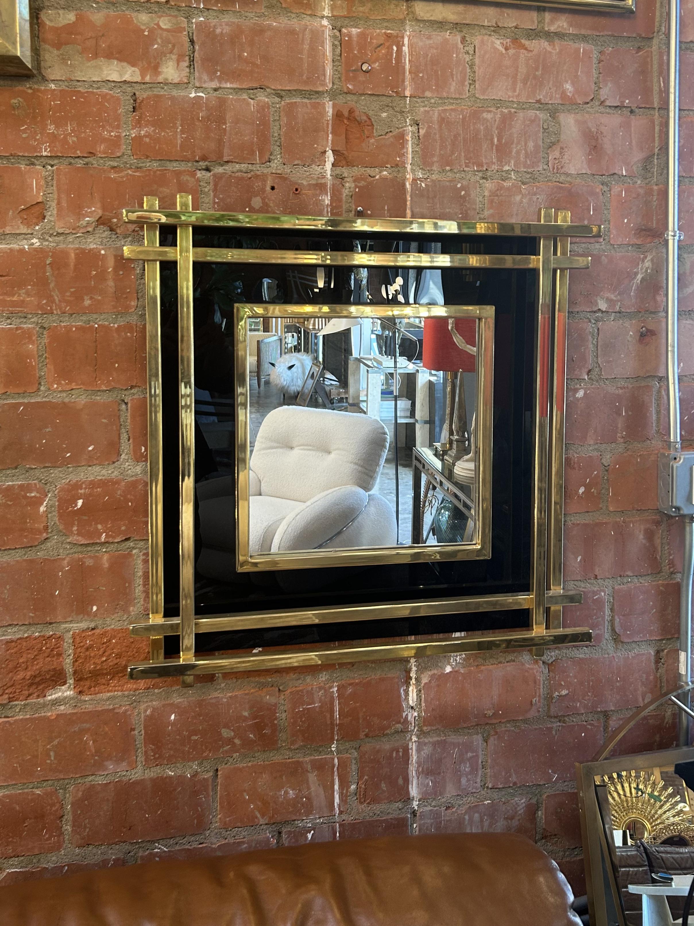 A bold and sleek Italian wall mirror from the 1970s, showcasing refined geometry and the luxurious materials typical of mid-century design. This piece features a layered composition of polished brass and high-gloss black backing, creating a