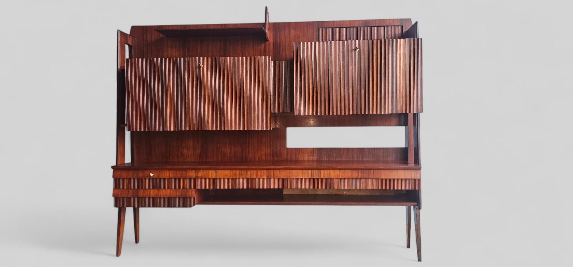 This multifunctional wall unit, which also serves as a bar, is a prime example of modern design from the 1960s. Its appearance features clean lines, functional elegance, and a keen attention to detail. Crafted from rich-colored teak wood with