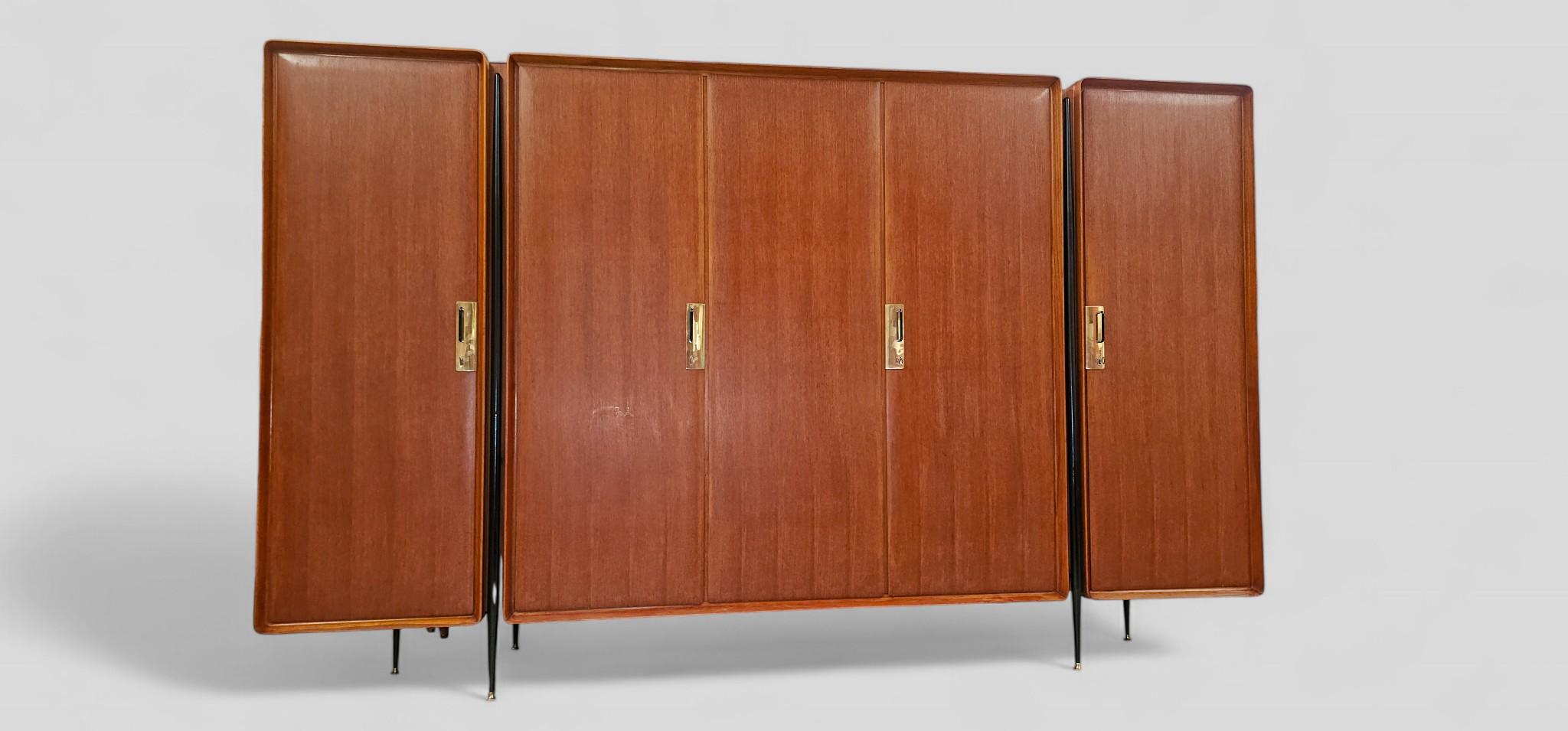 Armoire attribuée à Silvio Cavatorta, ce meuble se compose de sections verticales interconnectées reposant sur de minces pieds en métal noir avec des pointes en laiton. Fabriqué en teck, il présente un grain brun clair et des surfaces lisses. Les