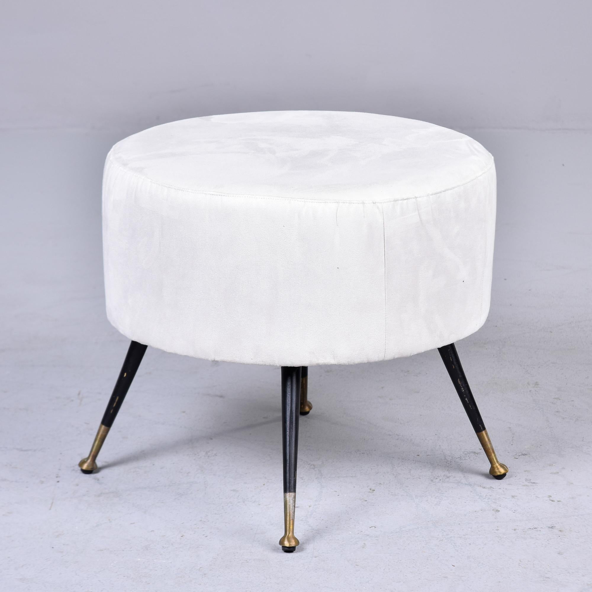 Found in Italy, this circa 1950s round stool has new white fabric upholstery. Four slender black metal tapered legs with brass feet. Unknown maker. Two available at the time of this posting. Sold and priced individually. 