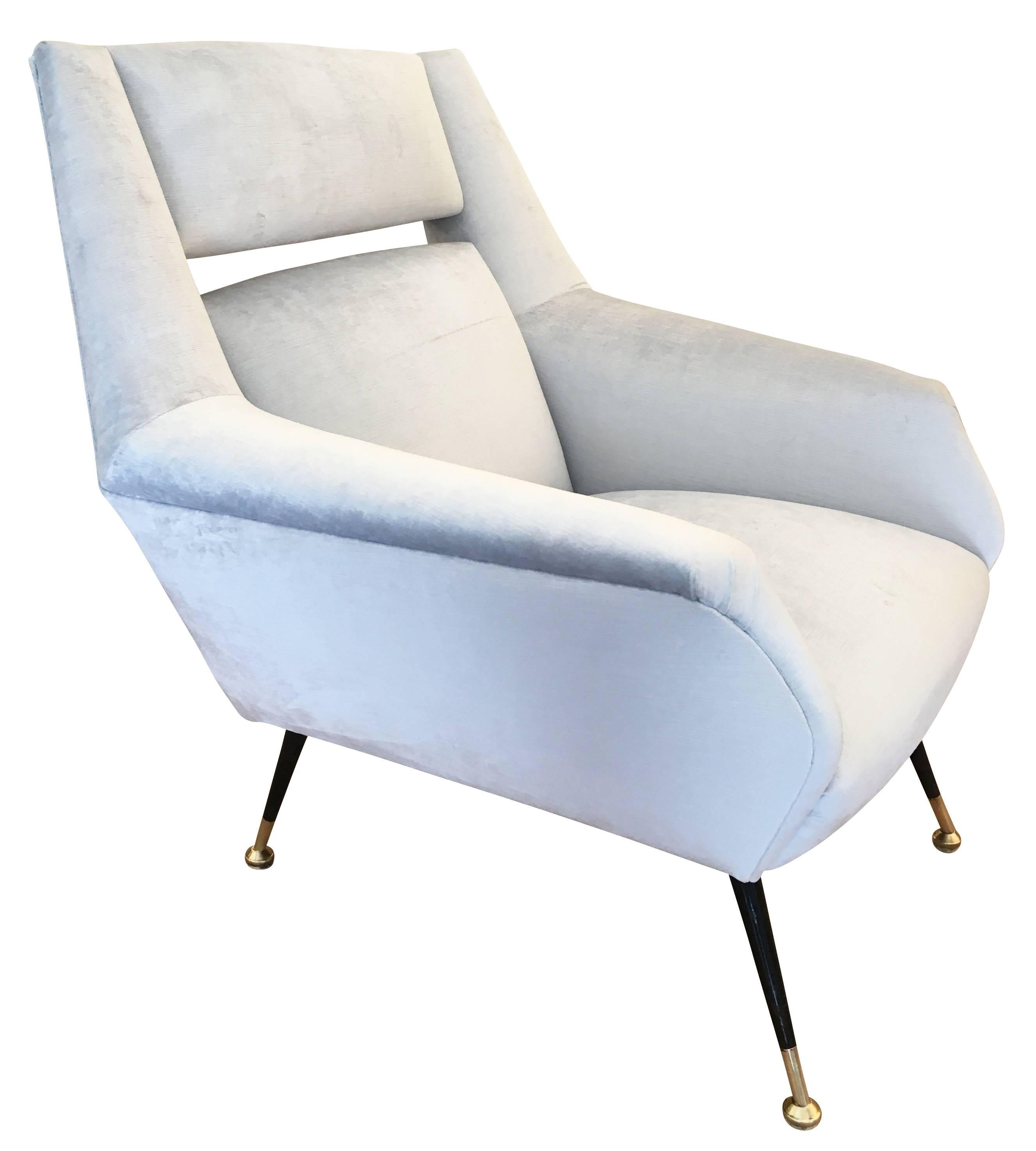 Chic Italian midcentury armchairs in the style of Gio Ponti with a slit back. The legs are lacquered black with brass feet. One has been re-upholstered in a light blue velvet for display purposes and the other is still with the original fabric. For