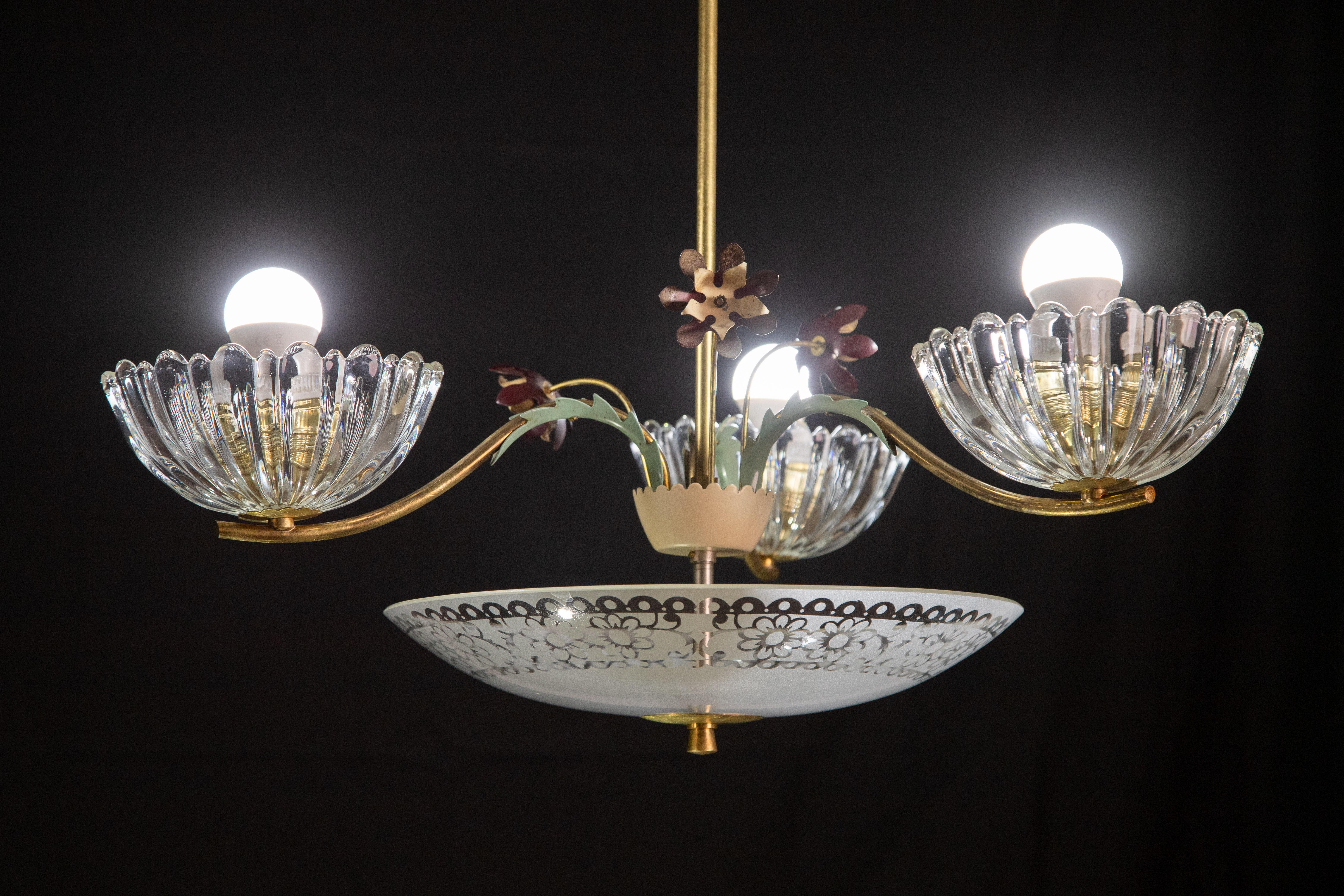 Gorgeous 1950s deco-era chandelier made of Murano glass and brass.

The chandelier consists of three glass bowls and a glass disk below, a brass frame decorated with three brass flowers.

It mounts three e27 lights.