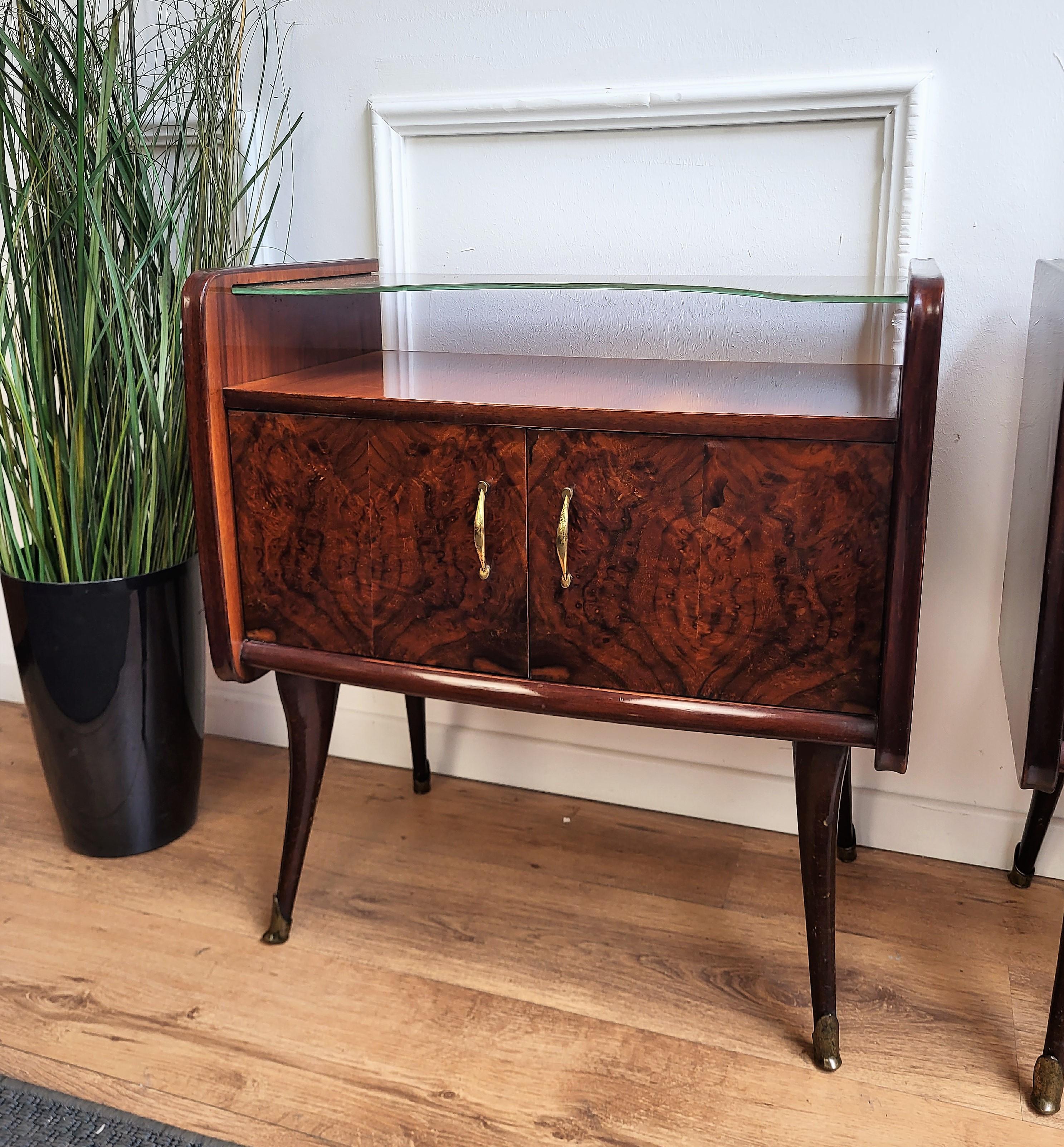 Very elegant and refined Italian 1950s Mid-Century Modern pair of bed side night stands tables in walnut veneer wood with front flip door and demilune glass top with brass details such as the handles and the 4 fluted legs finials. Those nightstands