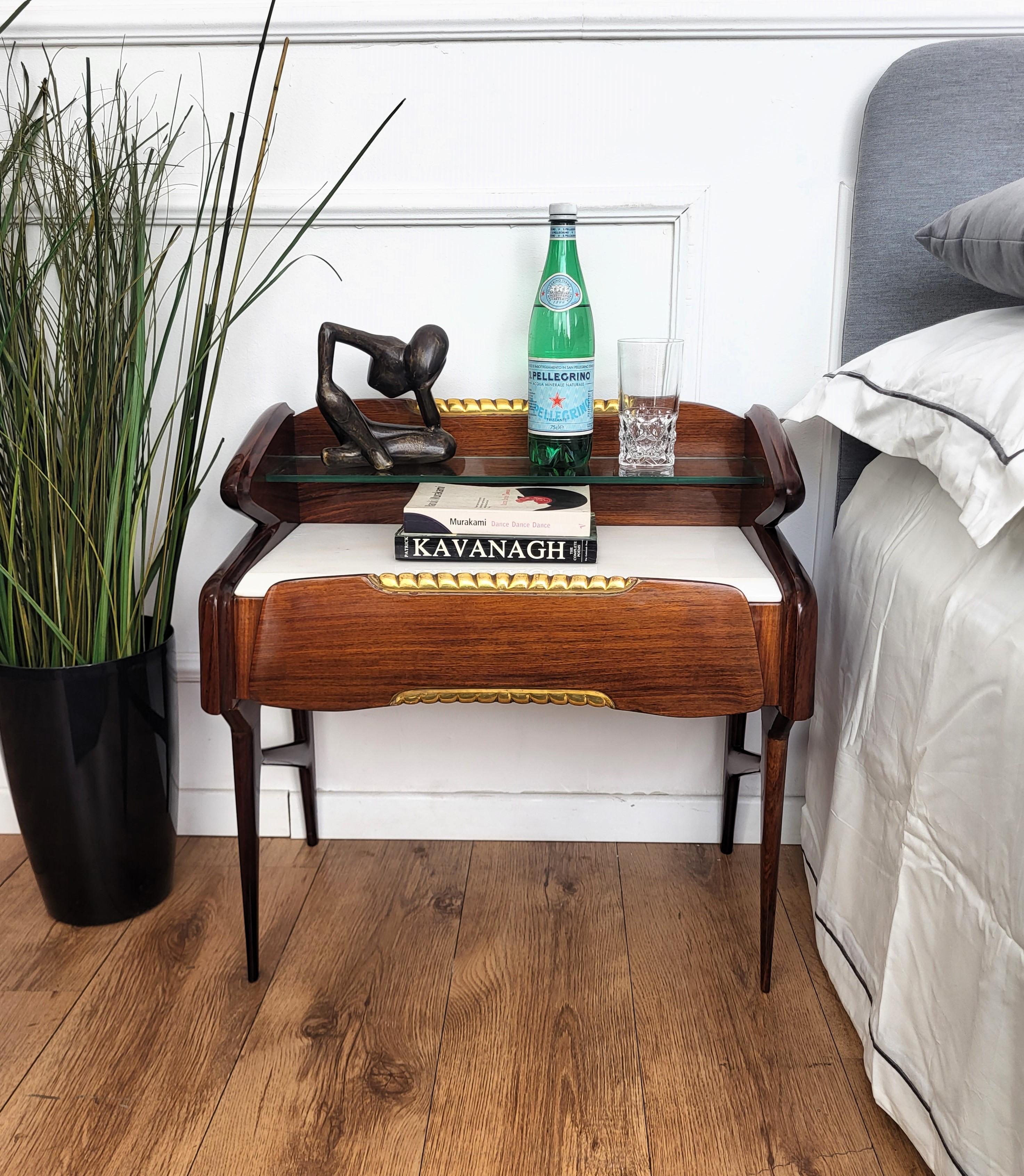 Very elegant and refined Italian 1950s Mid-Century Modern pair of bed side night stands tables in shiny wood with front drawer, white marble shelf and glass top shelf with gilt carved decor details. Those nightstands make a great look in any style