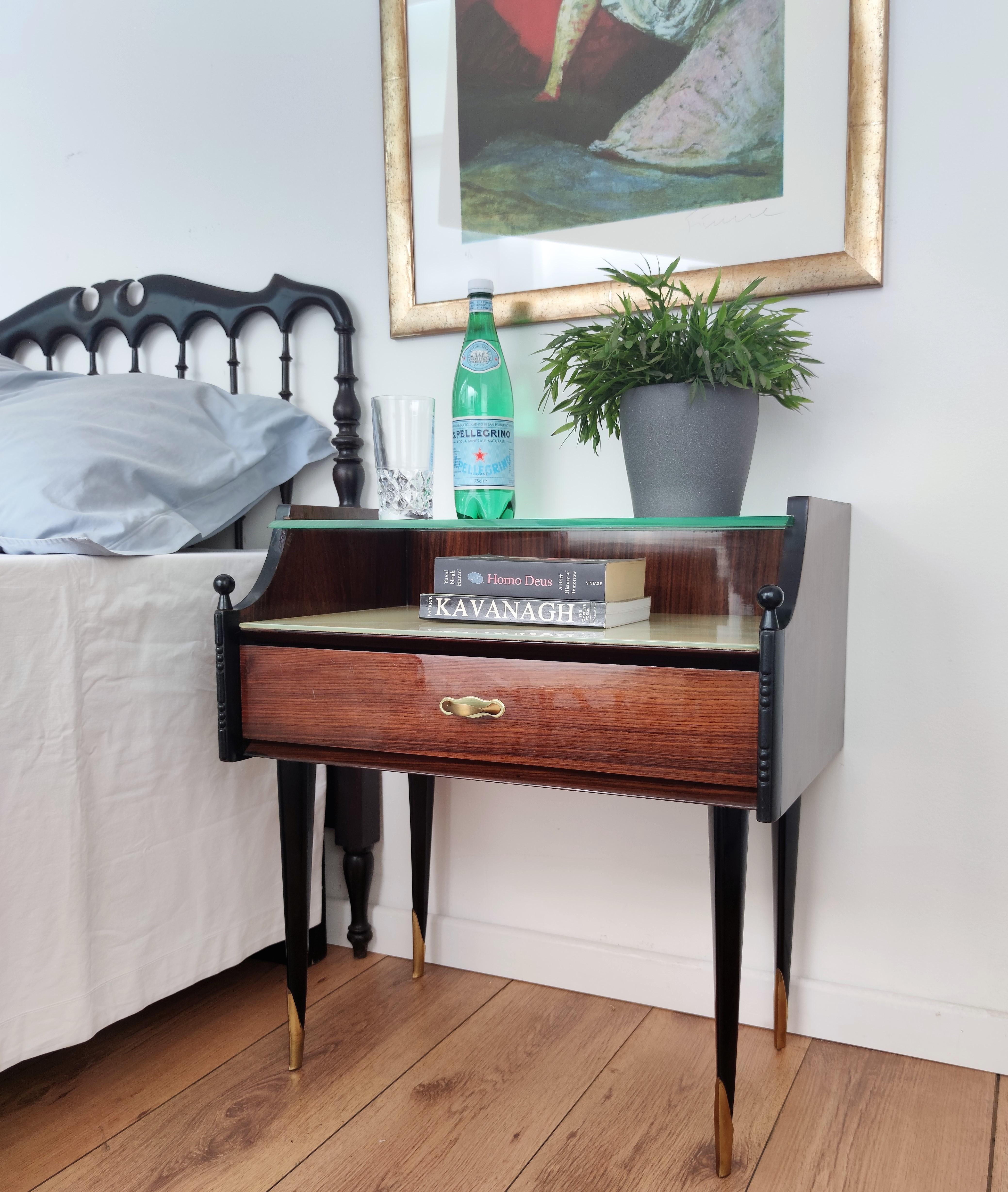 Very elegant and refined Italian 1950s Mid-Century Modern pair of bedside tables with walnut veneer wood front drawer, lacquered glass and second glass top with brass details such as the handles and decorated frame and legs. Those nightstands make a