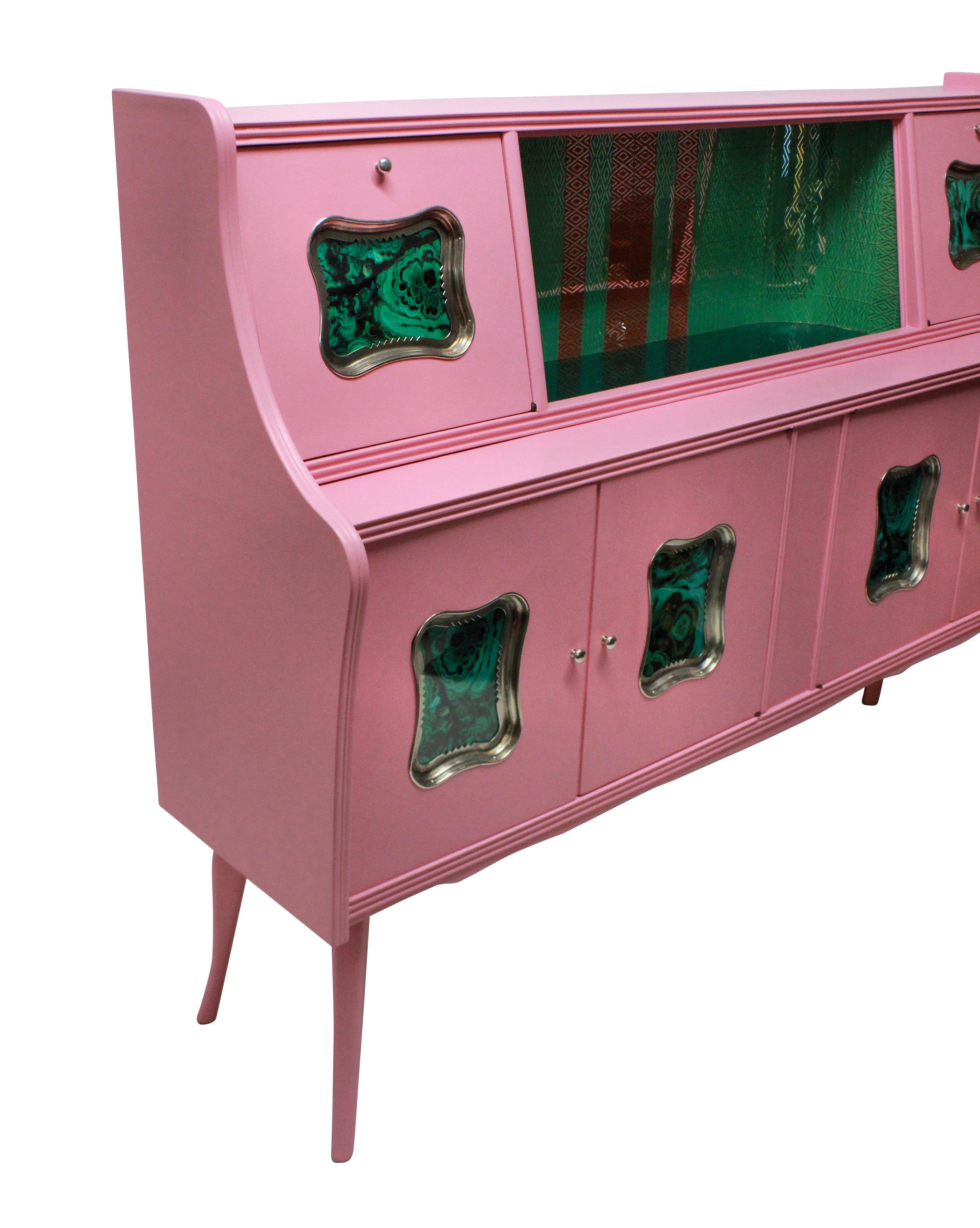 An Italian bar cabinet in pink lacquer, with a central green glass mosaic section, two drop down doors either side and cupboards beneath. With faux malachite panels in silver plated frames.

  