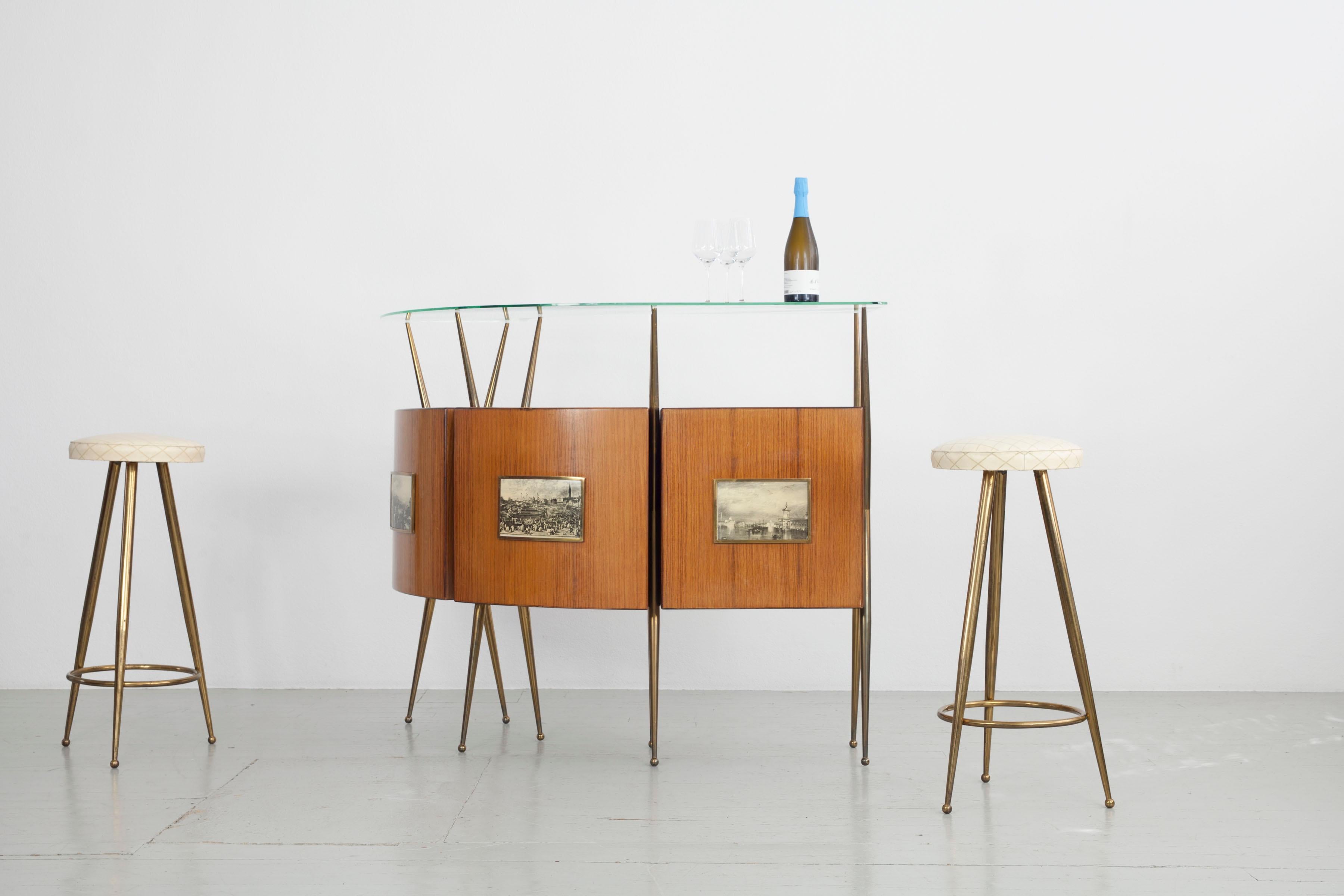 Italian 1950s home bar with bar cabinet and stools. This stylish mid-century bar has a beautiful curve in the rosewood wood cabinets, which feature 3 black and white prints of Venice. The bar stands on brass legs and the glass top above is also