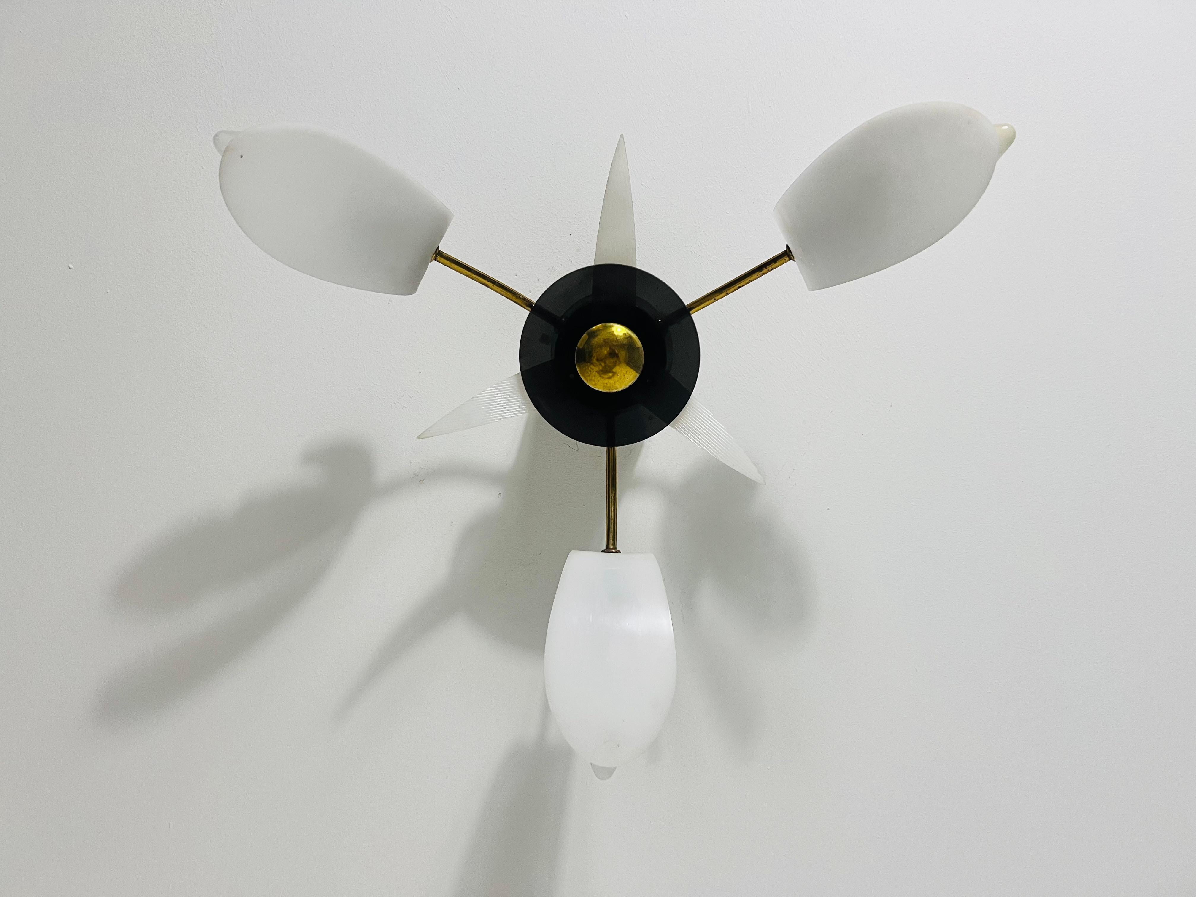 This Italian Sputnik ceiling lamp from the 1950s is a captivating example of mid-century modern design in the style of Stilnovo. Featuring three arms with white acrylic glass shades, black sockets, this lamp exudes a timeless elegance. Its Italian