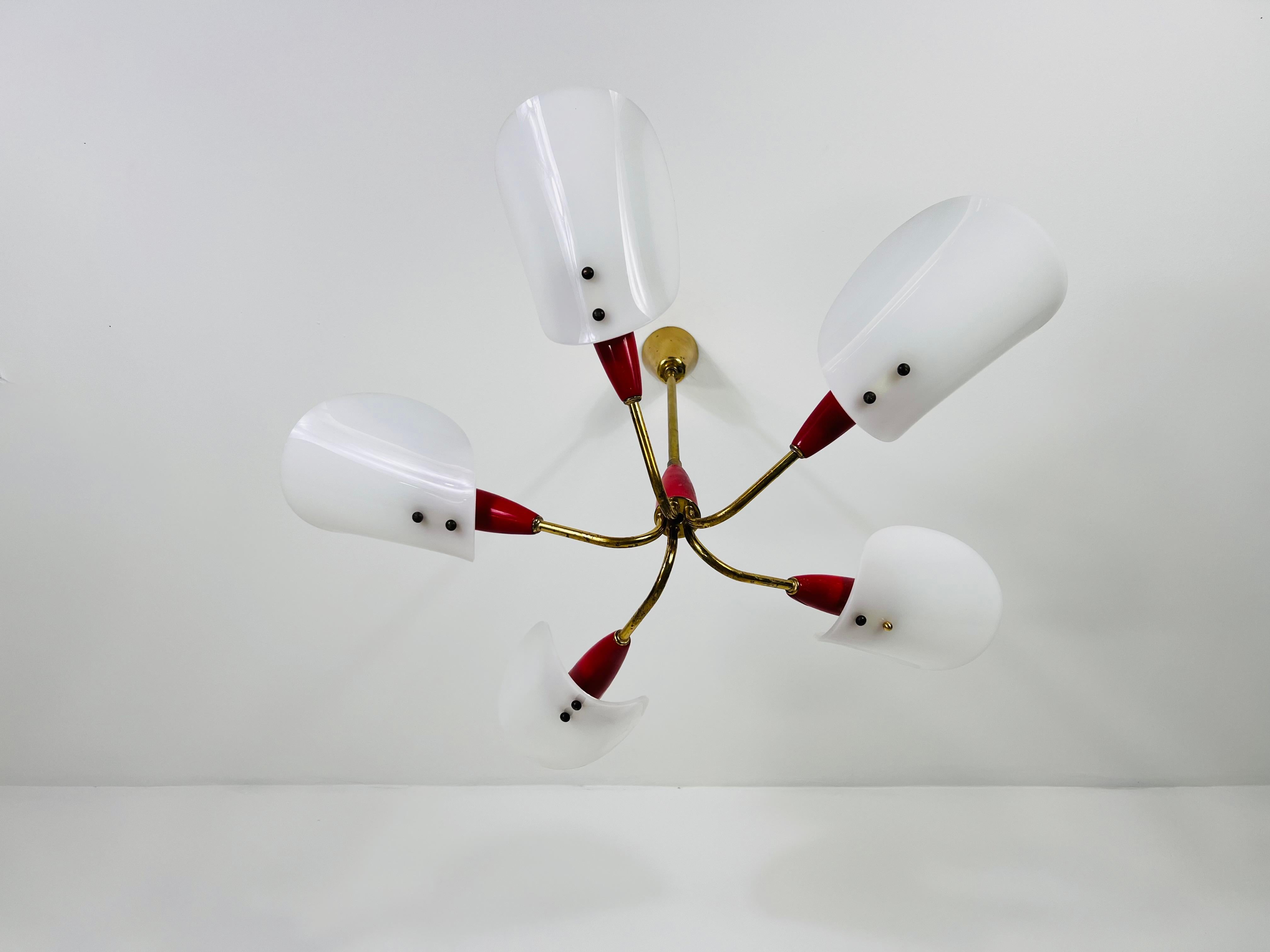 This Italian Sputnik ceiling lamp from the 1950s is a captivating example of mid-century modern design in the style of Stinovo. Featuring five arms with white acrylic glass shades, red sockets, and a brass rod with a brass canopy, this lamp exudes a