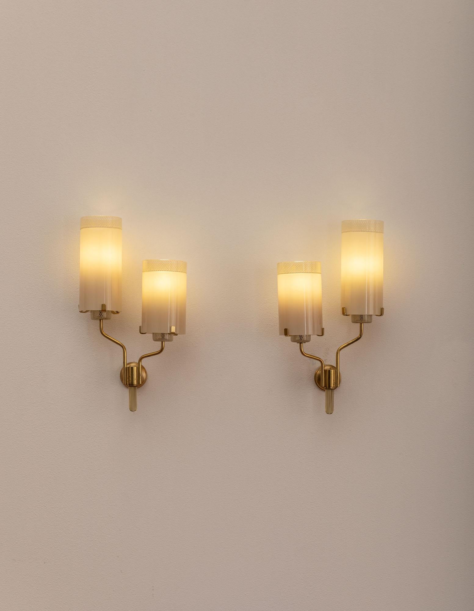 Pair of elegant sconces with refined brass details.
Each applique has two lights, composed by cylindrical Murano glass shades decorated with Reticello, a geometrical motif as the internal light holders. The thin brass arms have different lengths as