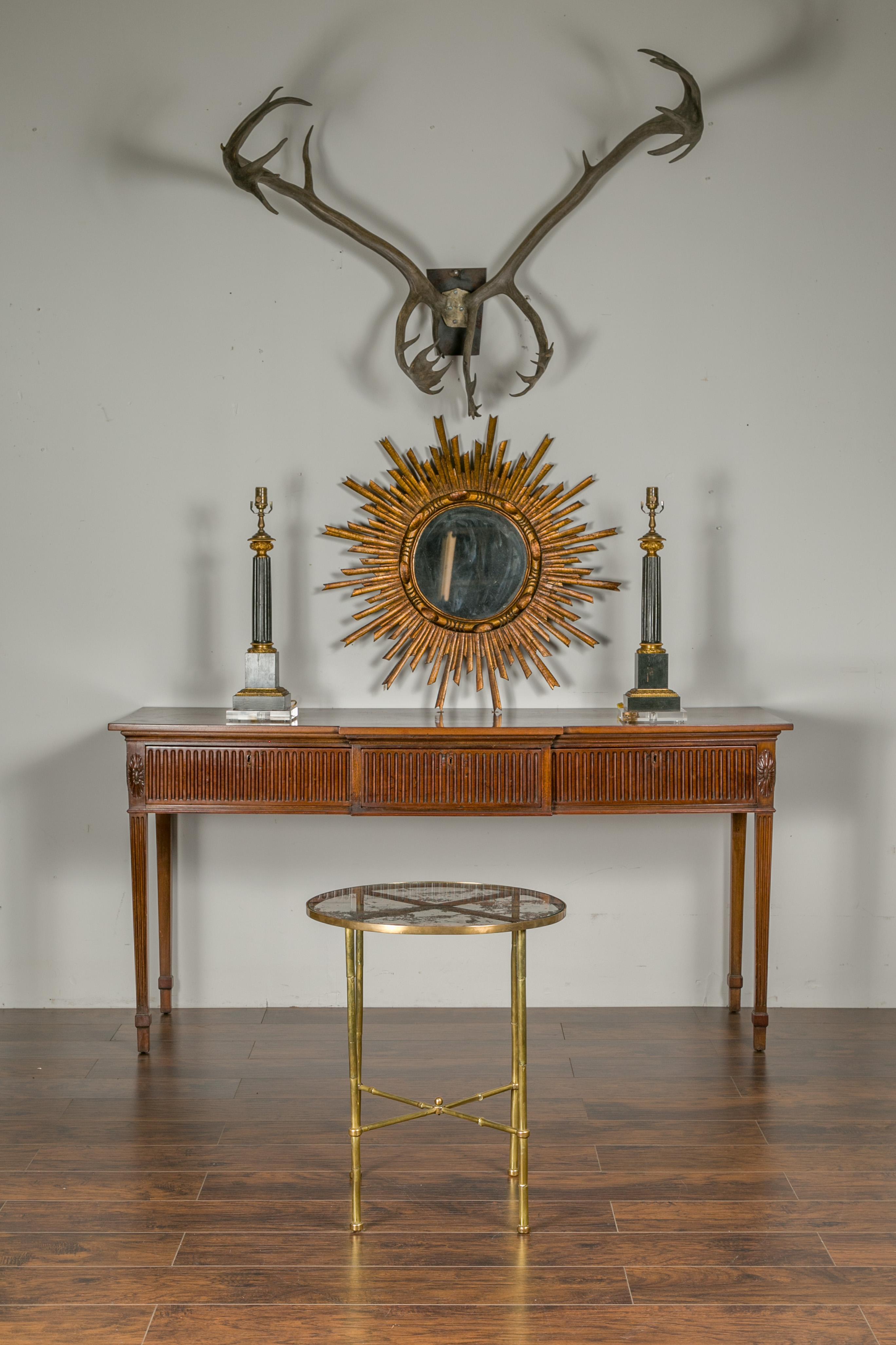 An Italian vintage brass round side table from the mid-20th century, with distressed glass top and X-form cross stretcher. Crafted in Italy during the midcentury period, this brass side table features a circular top adorned with distressed glass,