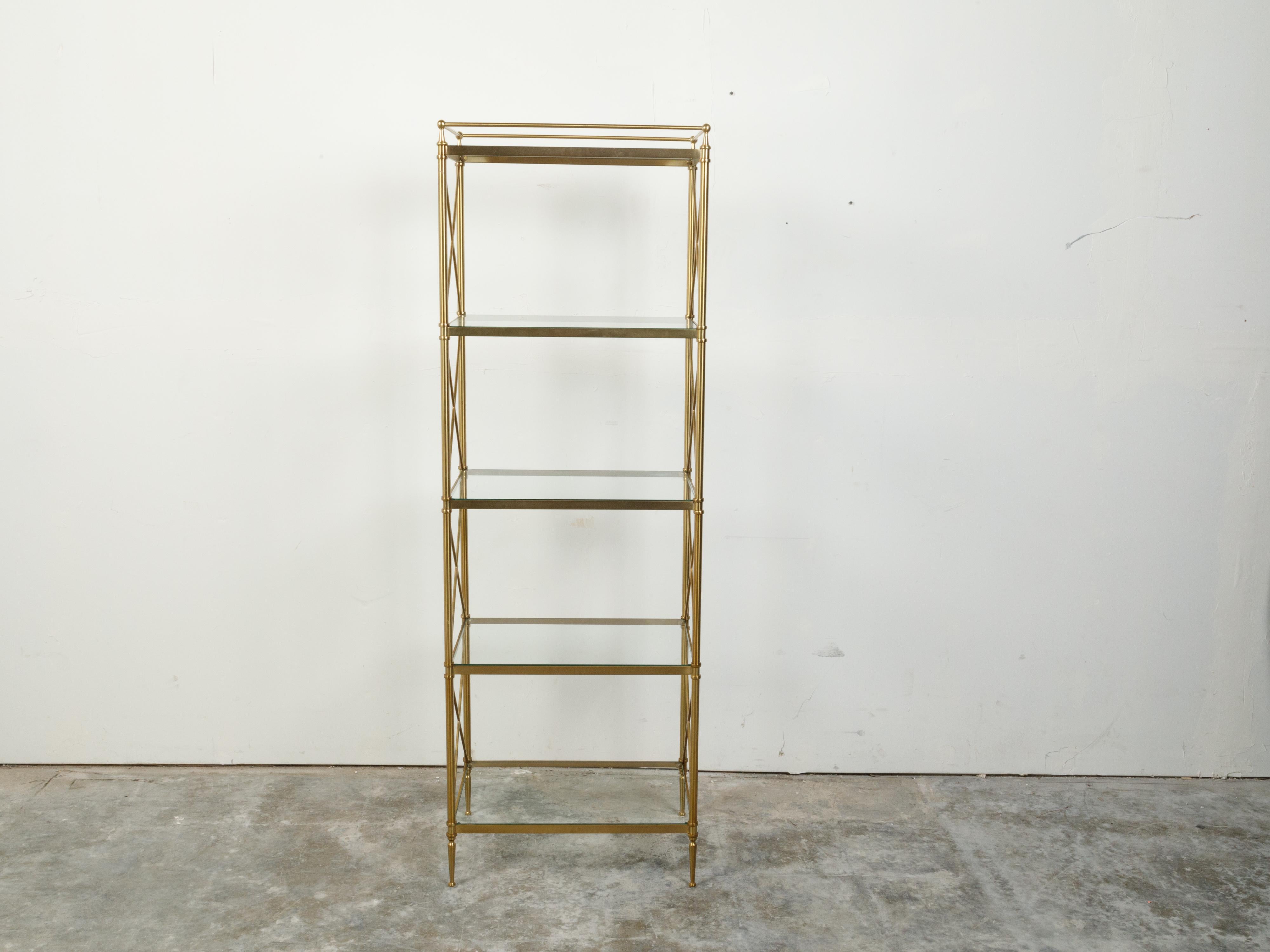 An Italian vintage brass bookshelf from the mid 20th century, with glass shelves and X-Form motifs. Created in Italy during the midcentury period, this narrow bookcase features a linear brass structure securing five glass shelves. Flanked with