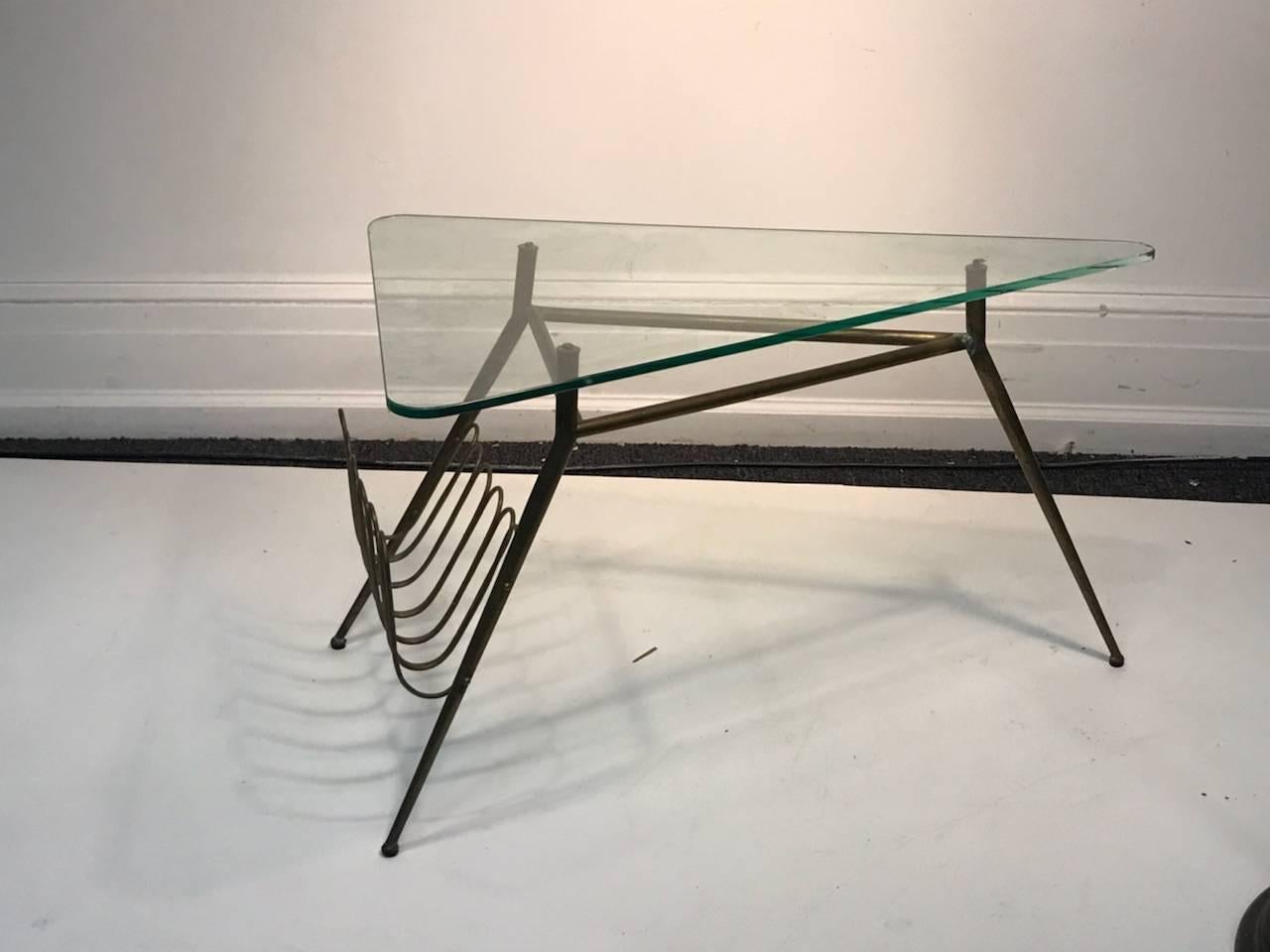 Modernist Italian brass tripod tapered leg base table with triangular glass top and angled brass magazine rack. Designed in The 1950s in Italy.