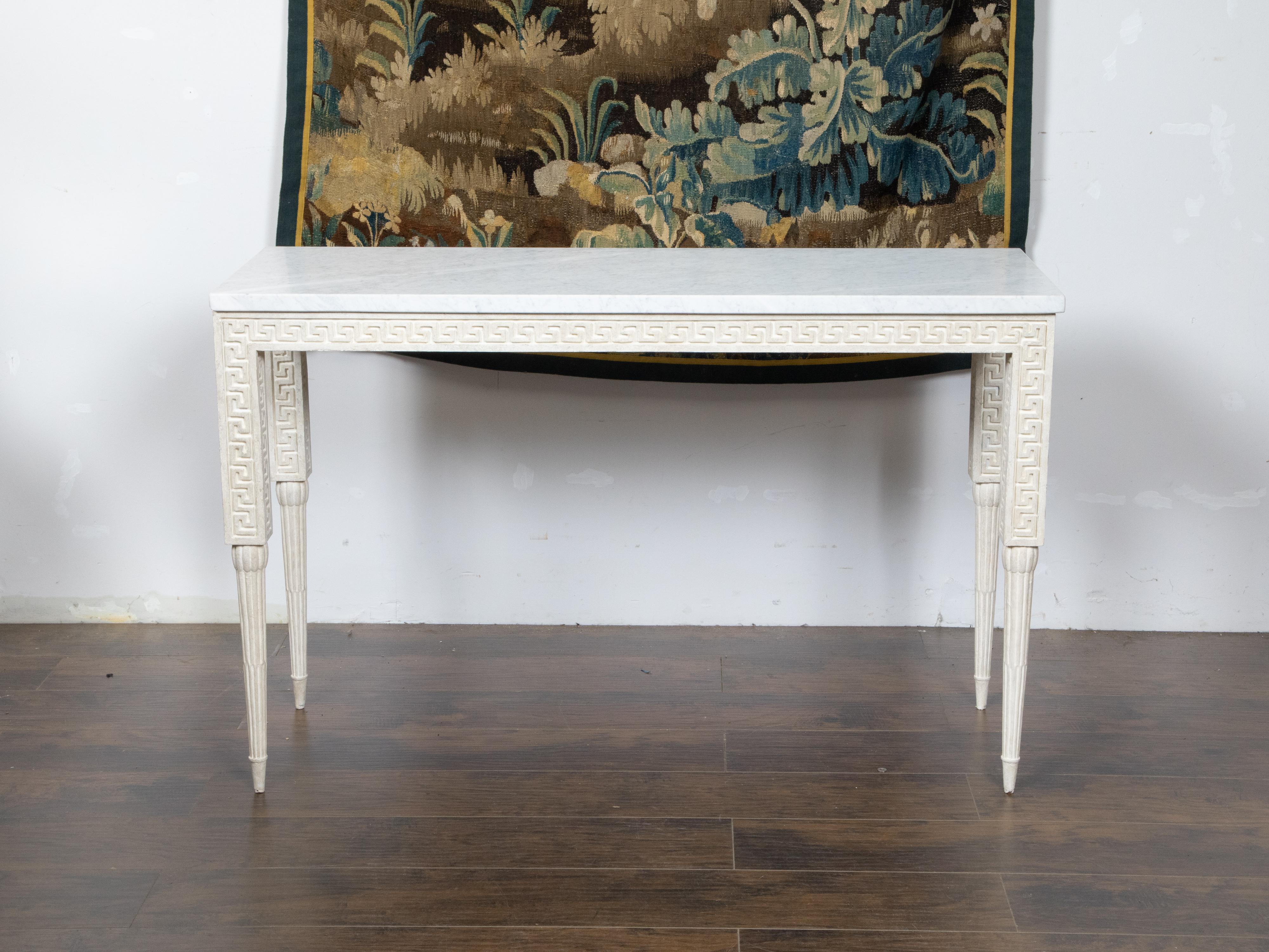 An Italian painted wood console table from the Mid-20th Century, with white marble top, carved Greek Key frieze and reeded tapering legs. Created in Italy during the midcentury period, this unusual console table features a rectangular white veined