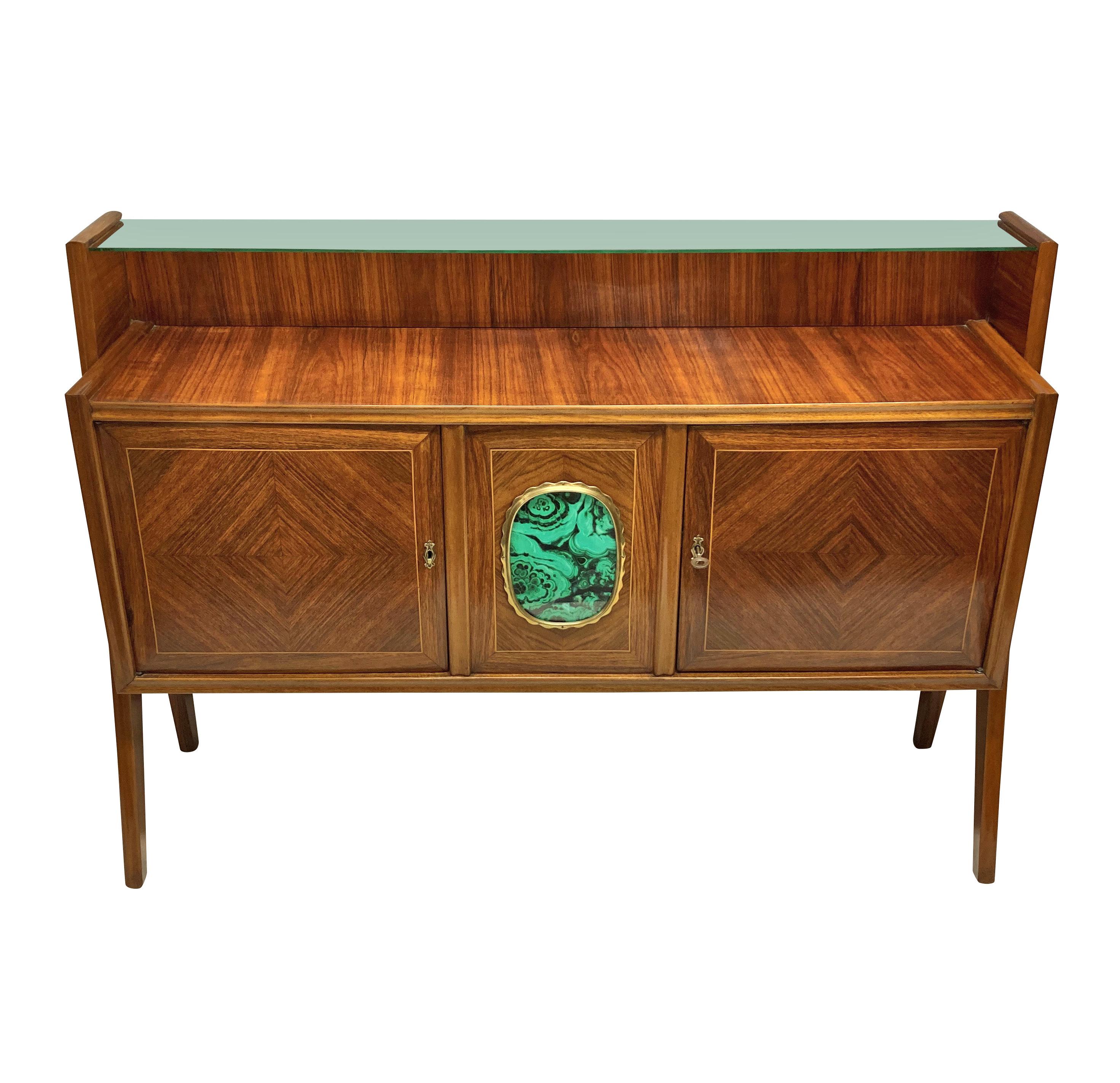 A stylish Italian Mid-Century credenza, beautifully veneered, with a central two door cupboard & upper glass shelf. The central panel with brass detailing and a faux malachite panel, supported each side with architectural legs.