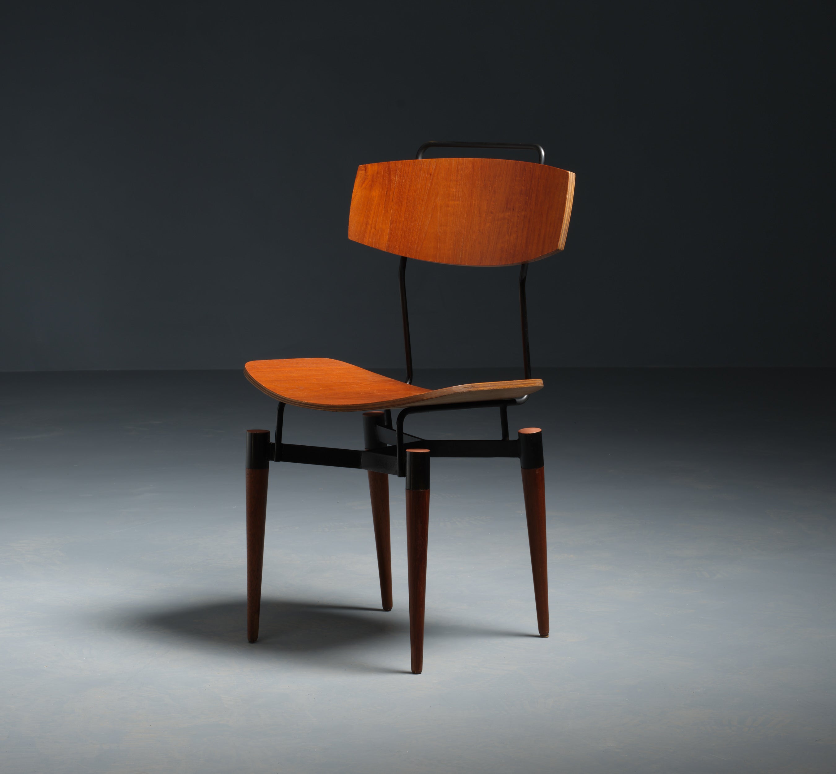 This Italian midcentury desk chair combines functionality with a minimalist aesthetic, characteristic of mid-20th-century design. Crafted from durable teak and accented with a black lacquered iron frame, the chair features clean lines and a sleek