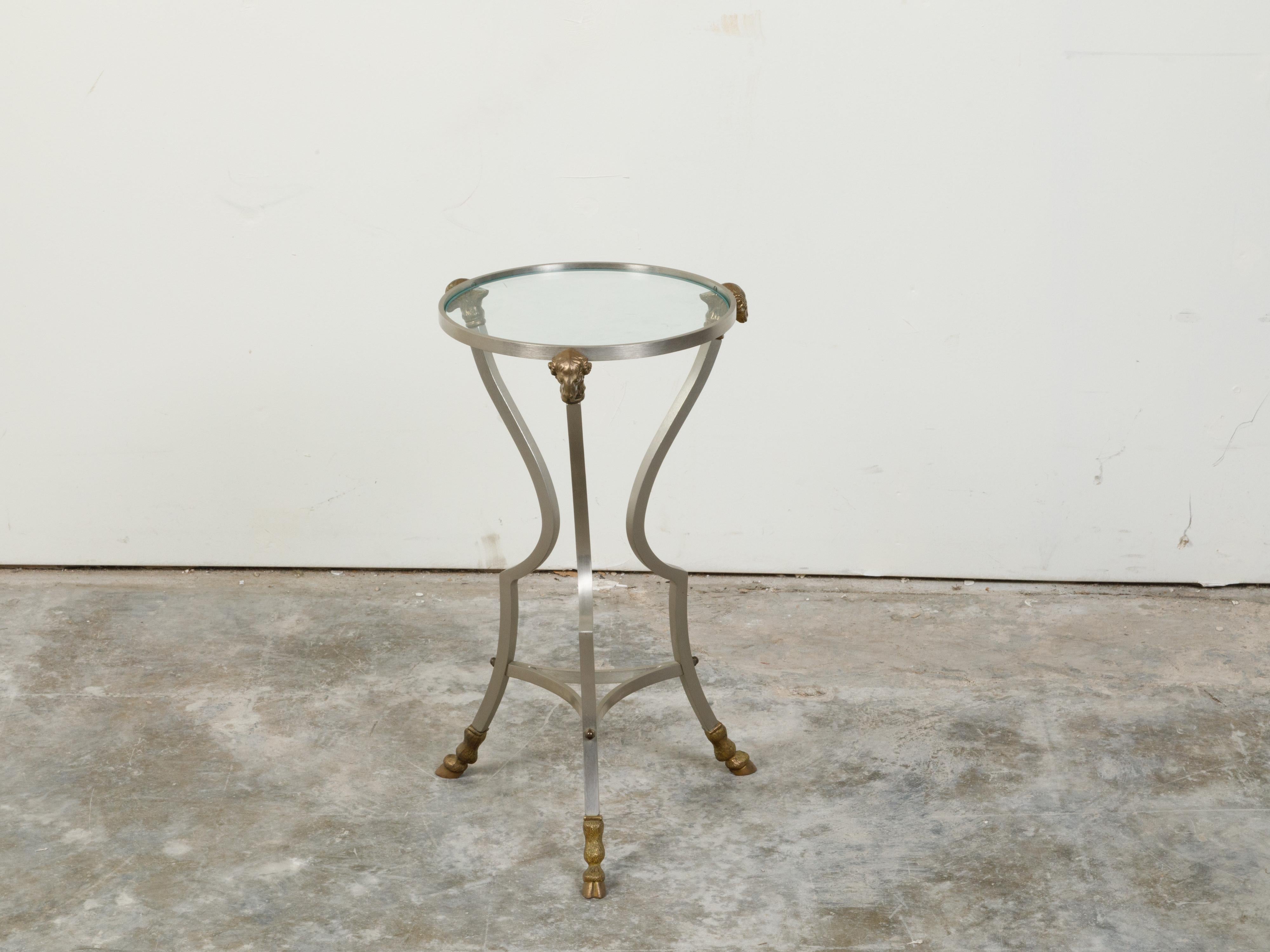 An Italian Directoire style vintage steel side table from the mid 20th century, with brass rams' heads and hoofed feet. Created in Italy during the midcentury period, this side table features a circular glass top supported by three rams' heads.