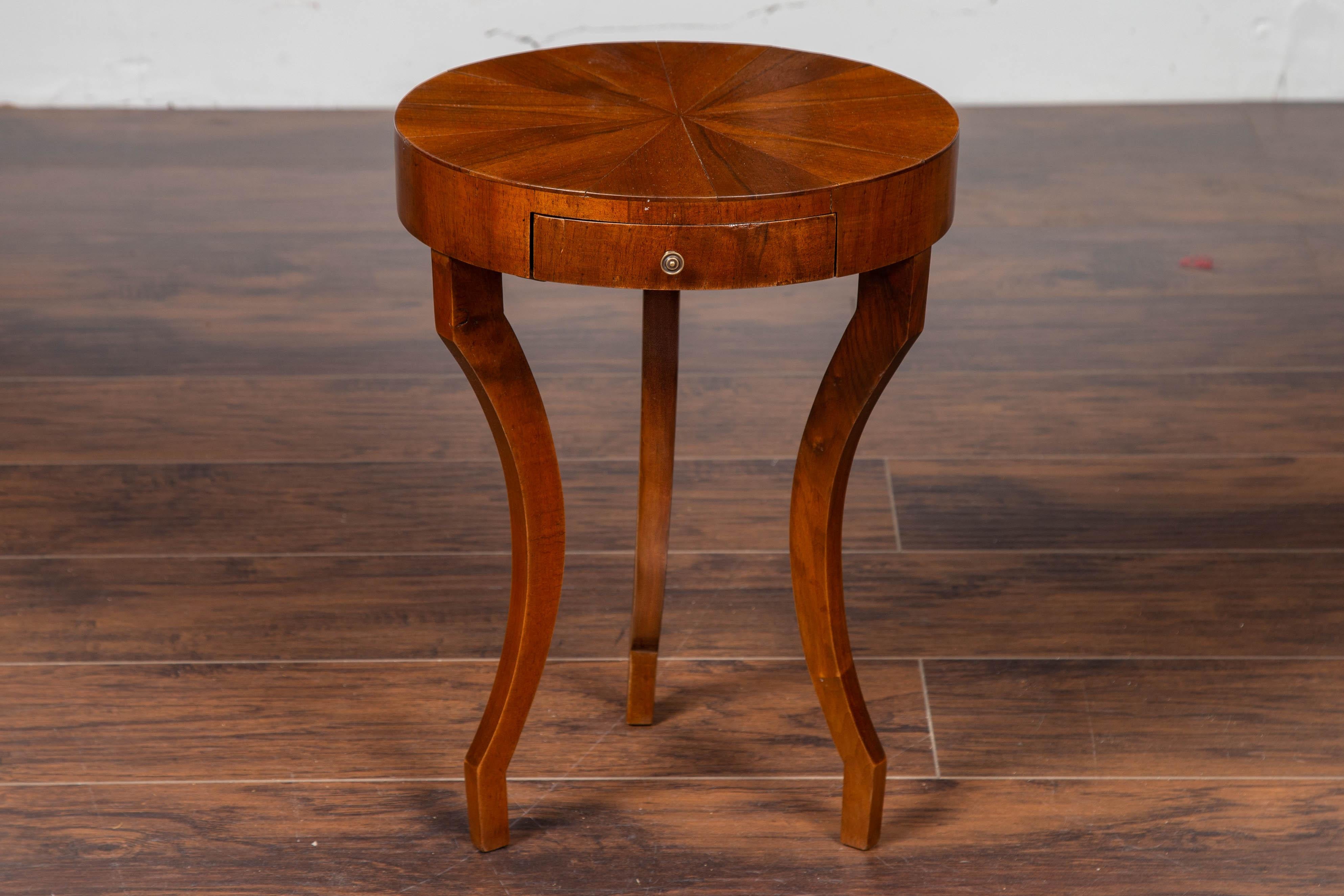 An Italian drink table from the mid-20th century, with radiating veneer and single drawer. Born in Italy during the midcentury period, this side table features a circular top adorned with radiating veneer, sitting above a single drawer fitted with