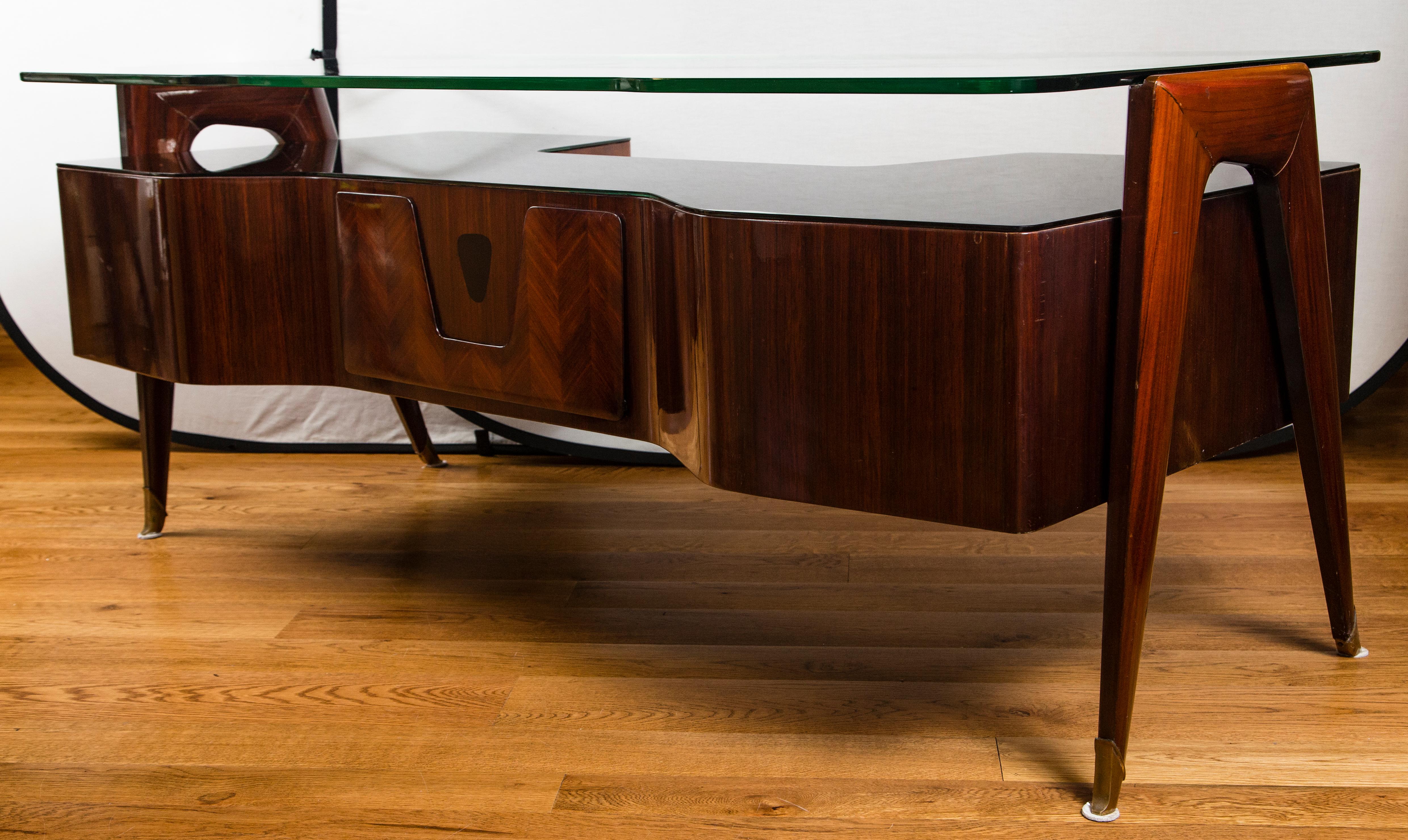 Stunning midcentury desk in rosewood, designed by Vittorio Dassi and produced upon order in Italy in the 1950s for professionals. The thick floating glass top rests on the desk legs while a thin black glass envelopes the top body of the desk,