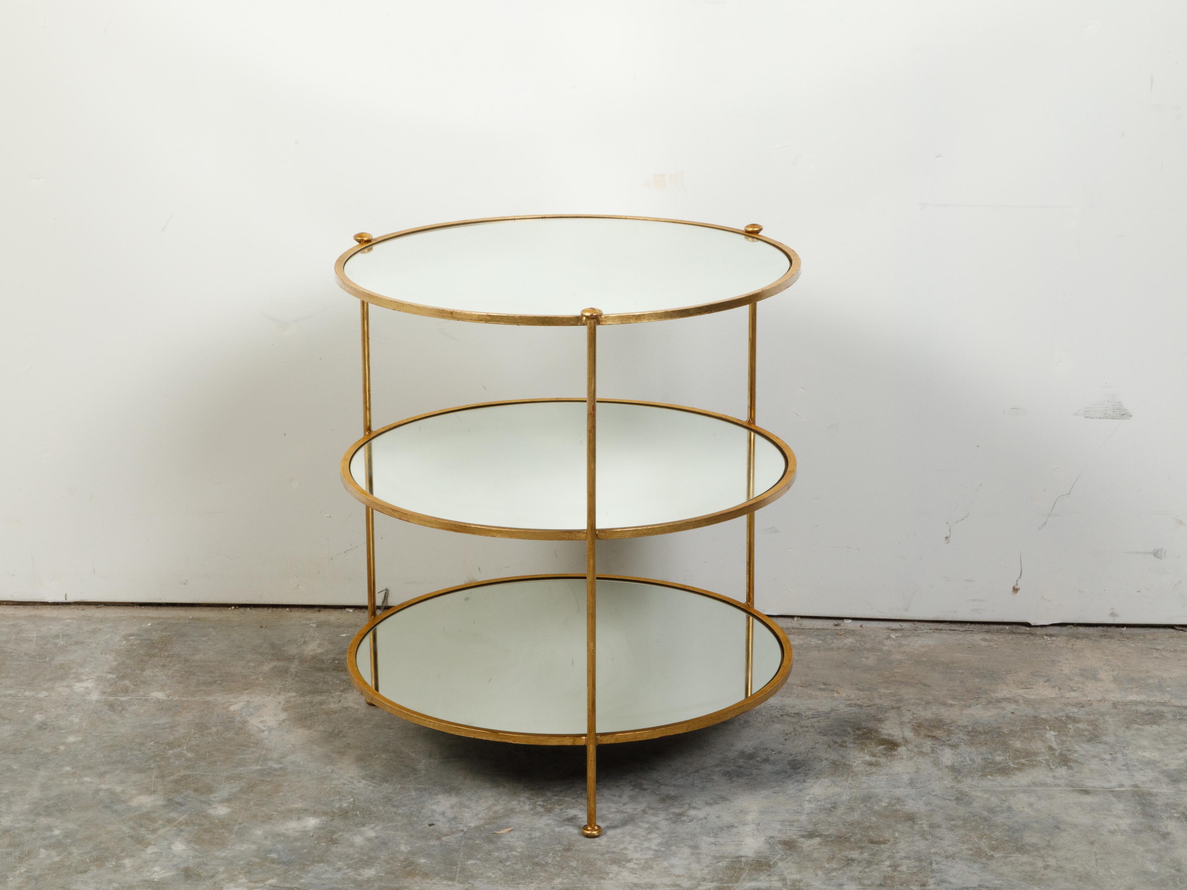 An Italian gilt iron three-tier side table from the mid 20th century, with round mirrored shelves. Created in Italy during the Midcentury period, this side table features three circular mirrored shelves secured inside a gilt metal structure. Raised