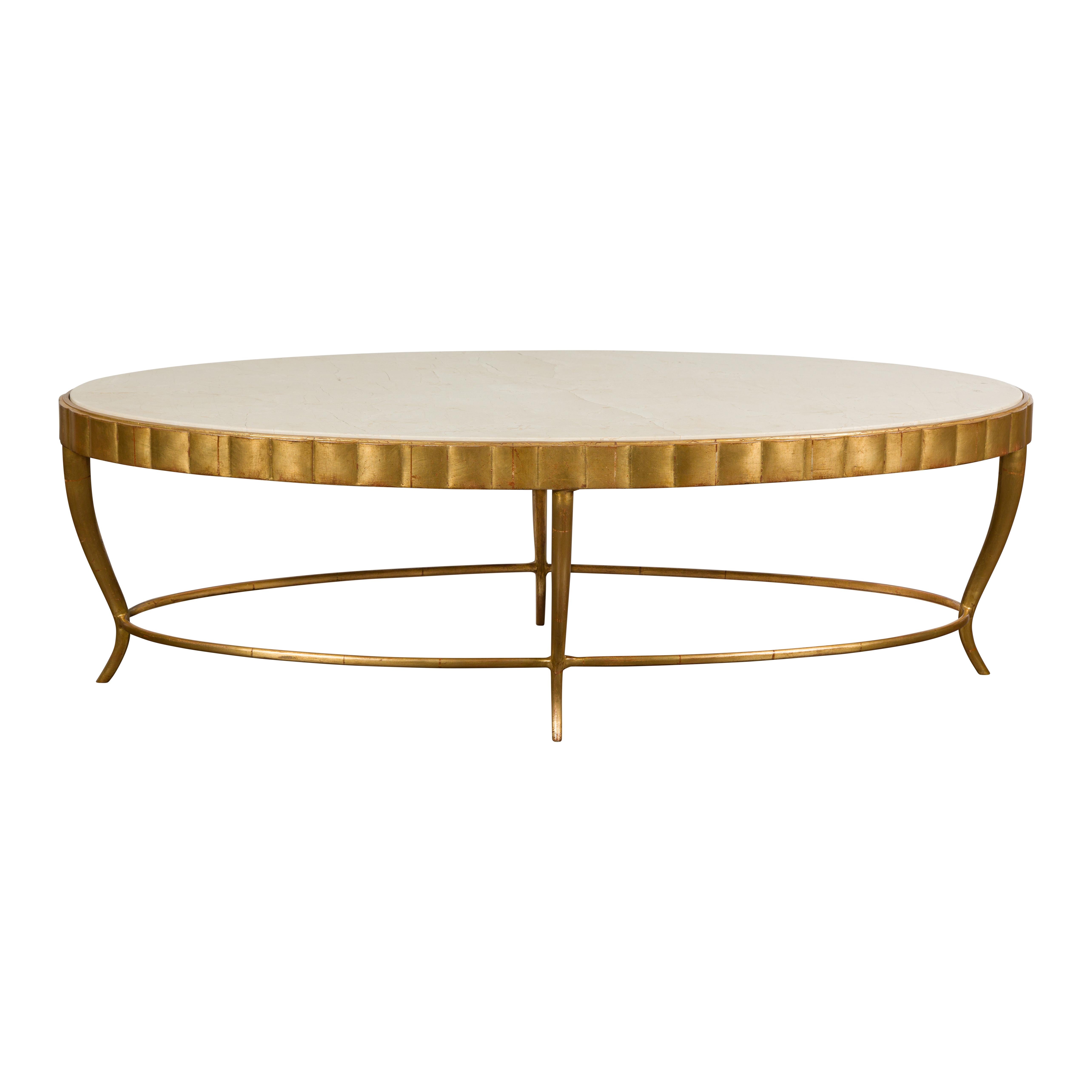 An Italian Midcentury gilt metal oval coffee table with cream colored marble top, reeded apron, curving legs and oval side stretcher. Add a touch of Midcentury elegance to your living space with this Italian gilt metal oval coffee table. Crafted