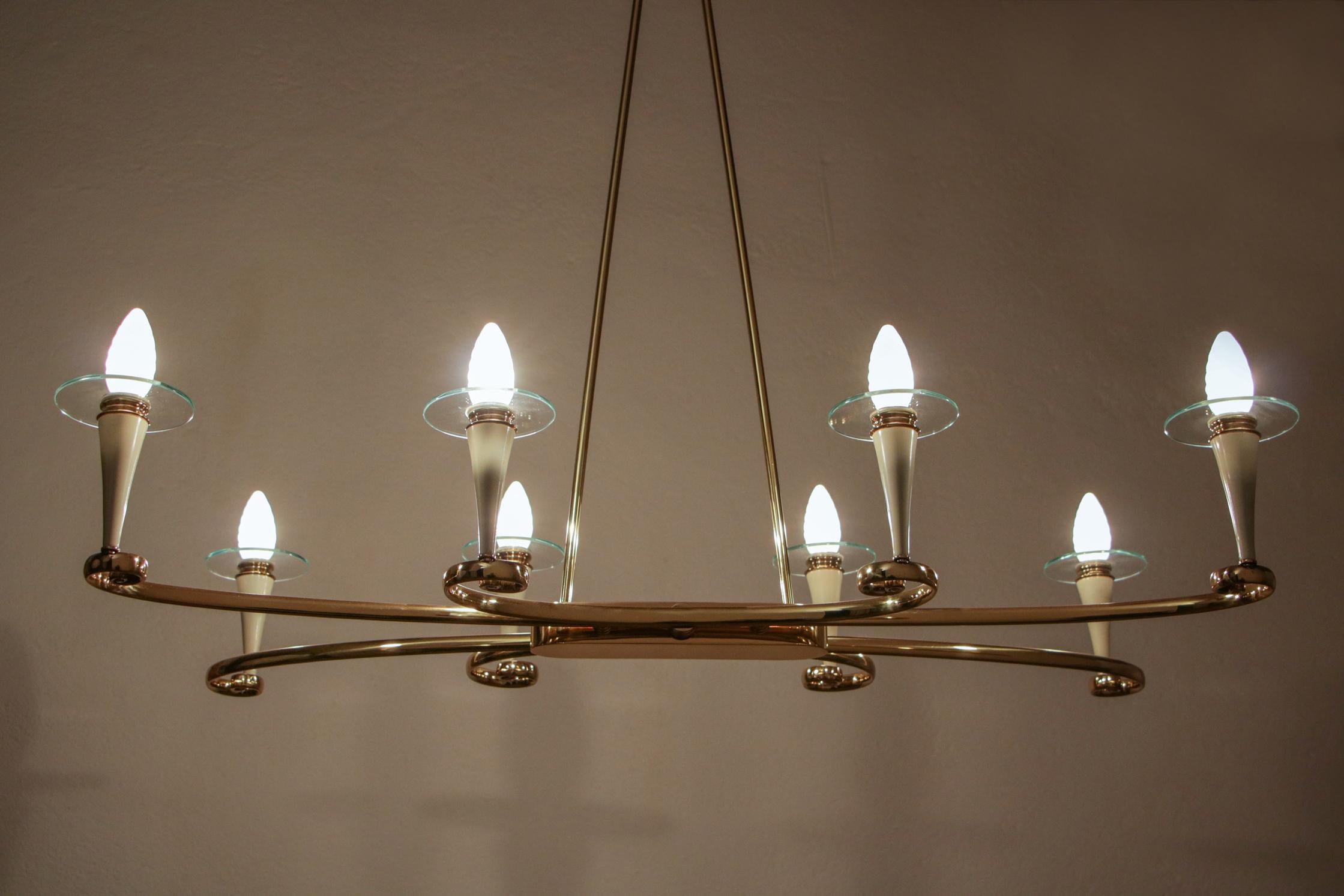 This wonderful Italian chandelier from the 1950s is a true masterpiece of design, featuring a clear-coated brass frame, ivory lacquered aluminum, glass, and eight E14 light bulbs. The main characteristics of this exquisite chandelier are refinement