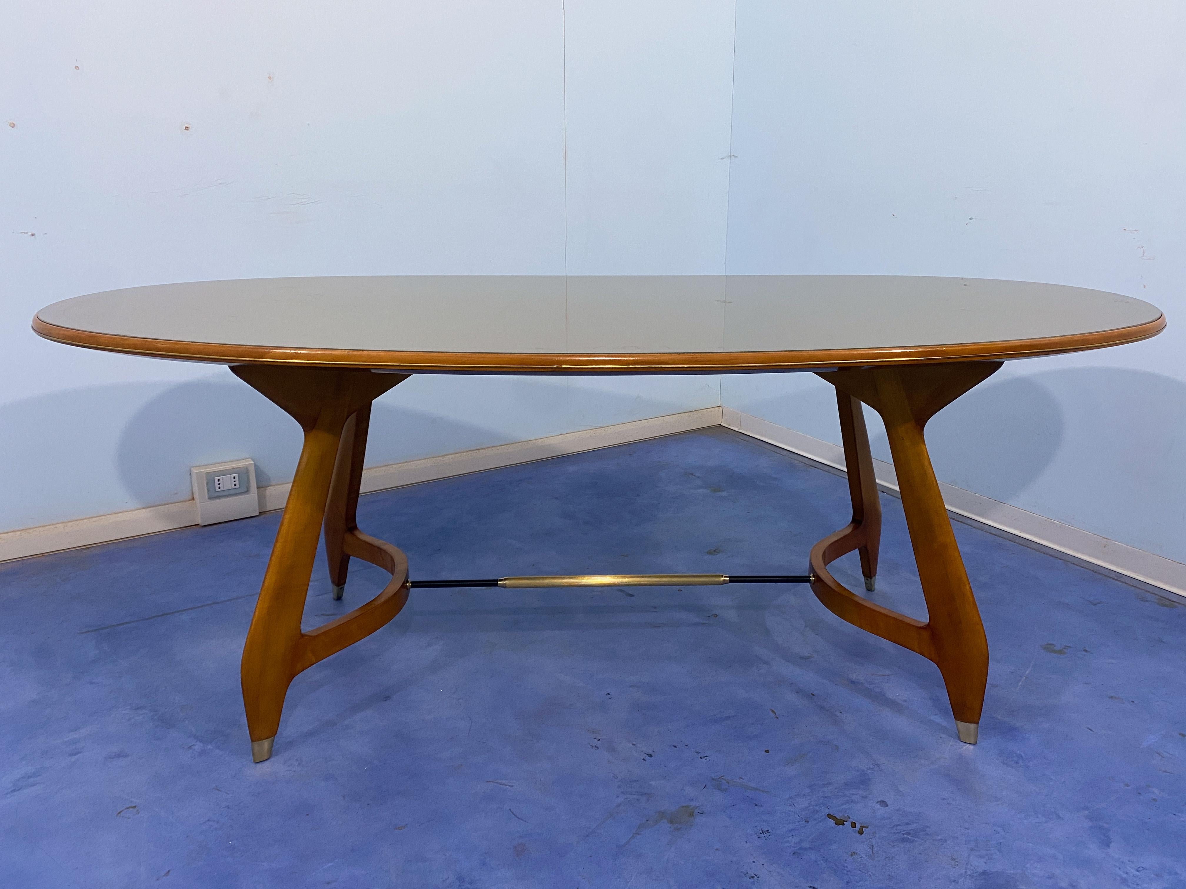 This midcentury oval dining table is a refined and elegant piece of furniture produced in Italy during the 1950s and attributed to Augusto Romano. The table has a top made of green glass, which is beautifully adorned with a decorative scroll border.