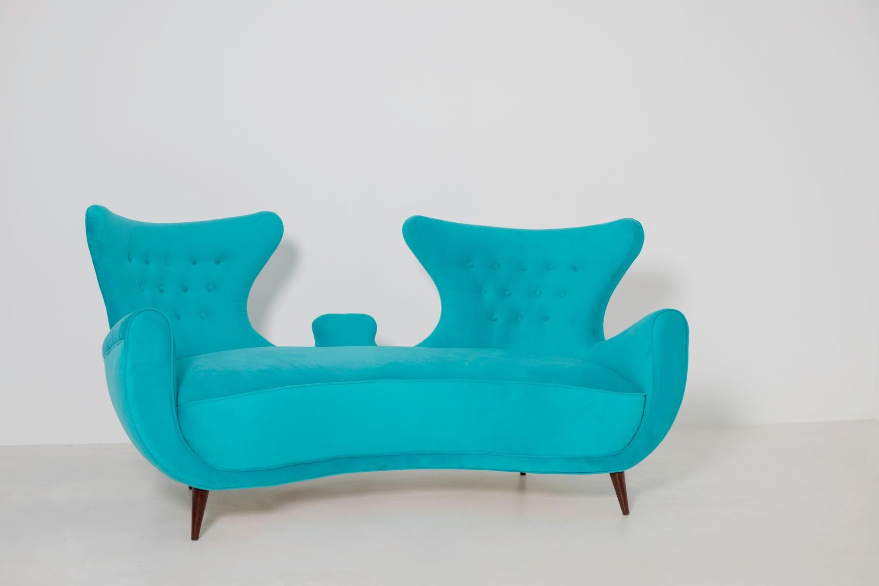 Elegant Italian loveseats sofa from the mid-last century. The pair of sofas has been restored in an elegant and refined Italian blue velvet. The peculiarity of the seat is its double and enveloping semi curved backrest which gives a perfect harmony