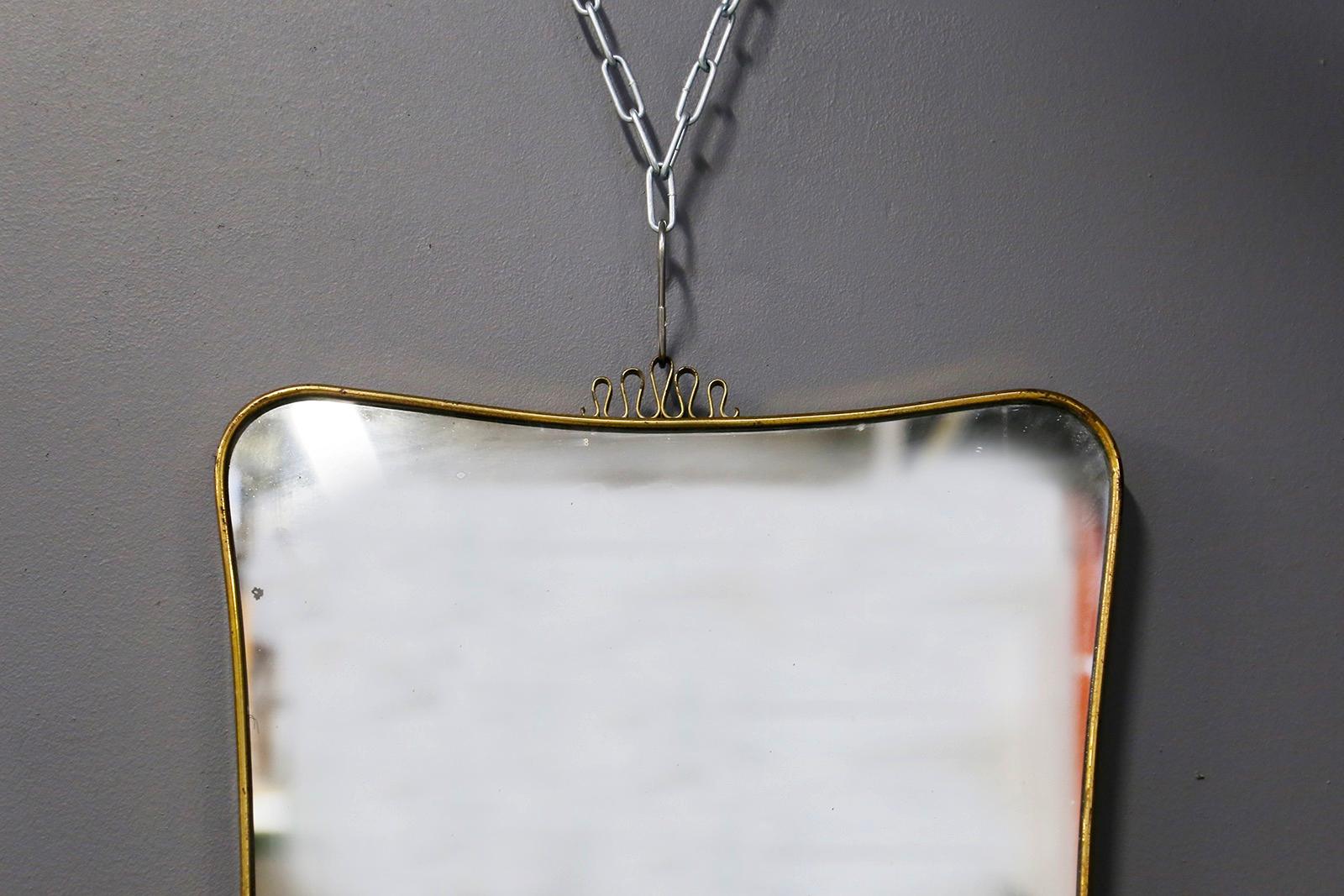 Elegant Italian wall mirror from the 1950s attributed to Gio Ponti.
The mirror is made of curved brass with slight wear due to age and use. In the upper part there is an ornamental element in curved brass, this decorative element is also found in
