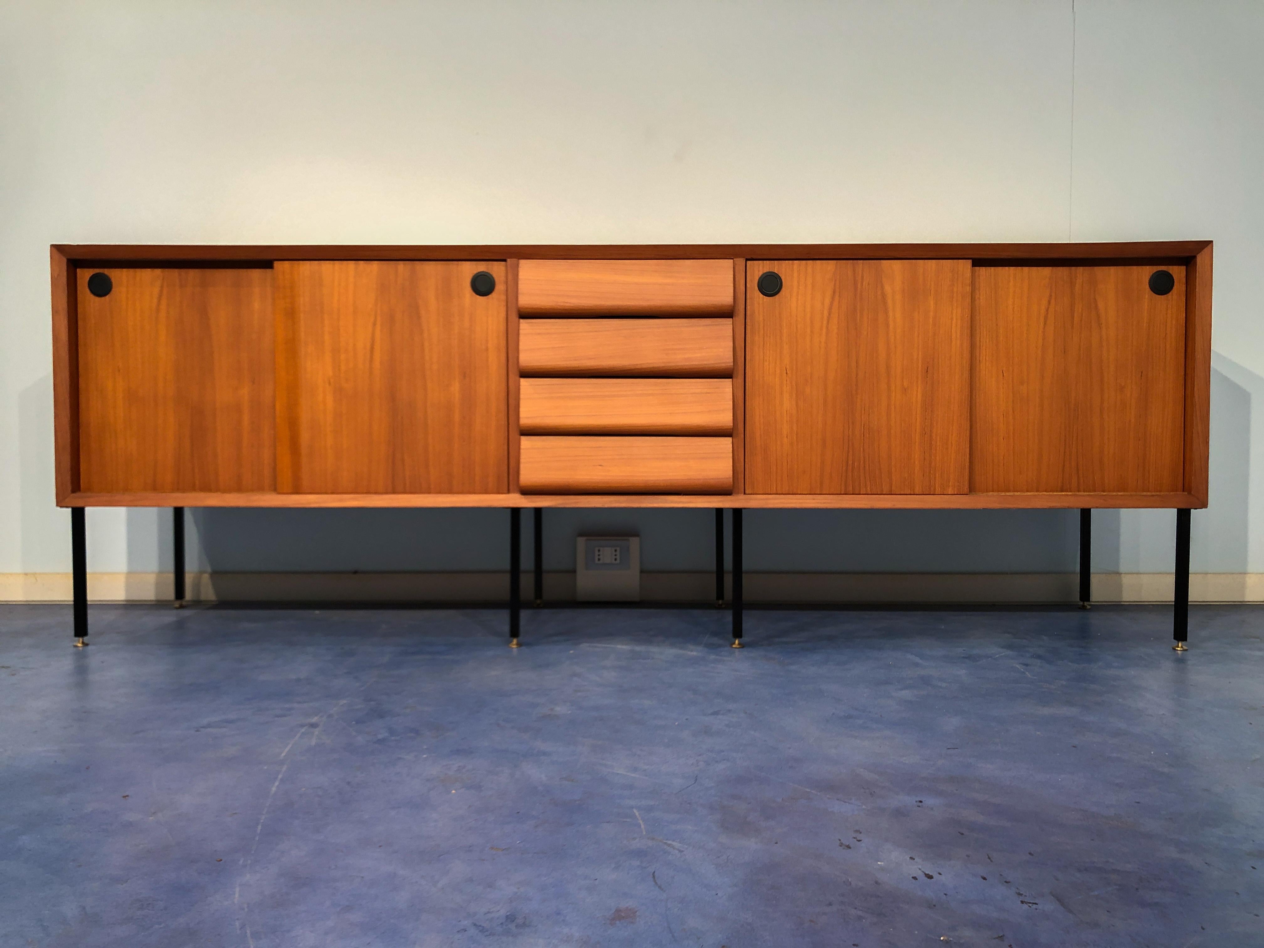 Beautiful Italian Mid-Century Modern teak sideboard with ample storage space within. Its large compartments with shelves hidden behind sliding doors, four drawers in the center with sophisticated design. The sideboard is supported by metal legs