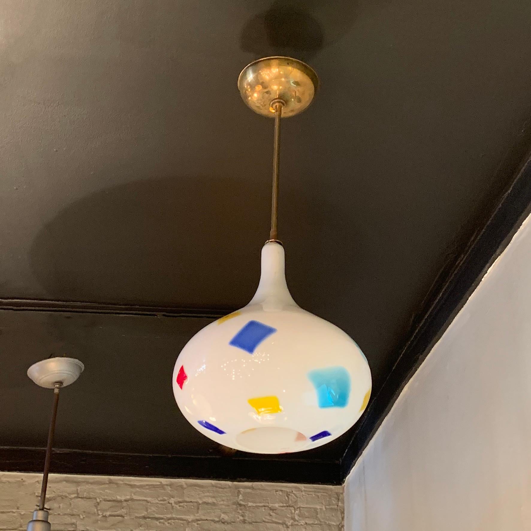 Italian, Mid-Century Modern, Murano glass pendant light attributed to Anzolo Fuga for AVeM (Artistica Vetreria Murano) features an onion shaped, white opaque glass shade embedded with patches of color on a brass pole with ceiling canopy, wired to