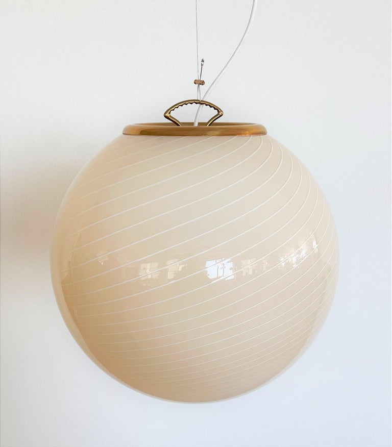 Beautiful and big elegant Murano glass globe pendant lamp with brass details.
Made in Italy in the 1970s.
Regular fine stripes in white color are worked into the light cream-yellow Murano glass. The glass globe is entirely hand-craftet.
The brass